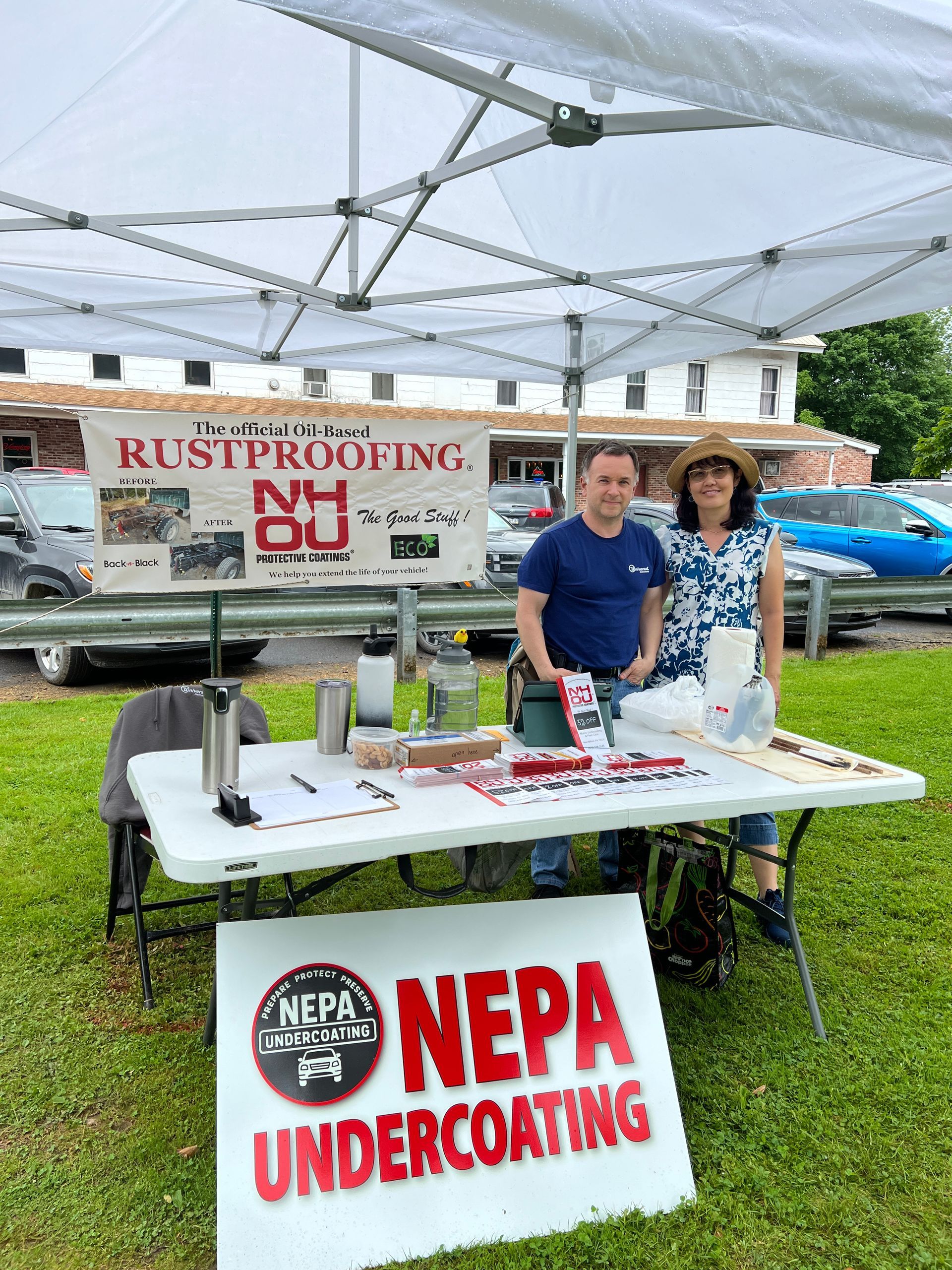 Two people at a NEPA Undercoating booth under a canopy, with banners and a table display.