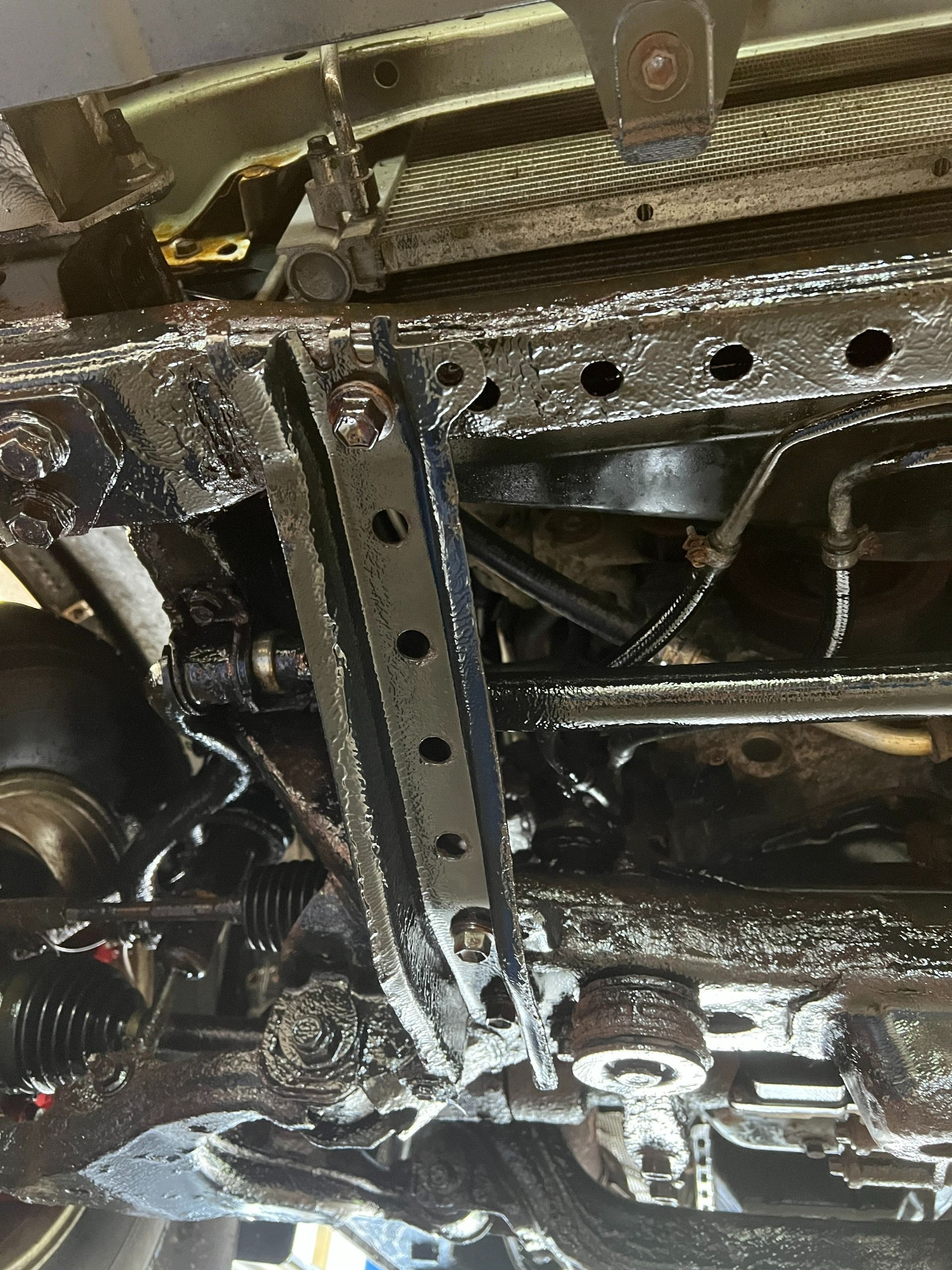 Undercarriage of a vehicle with exposed metal frame, bolts, and suspension components covered in grease.