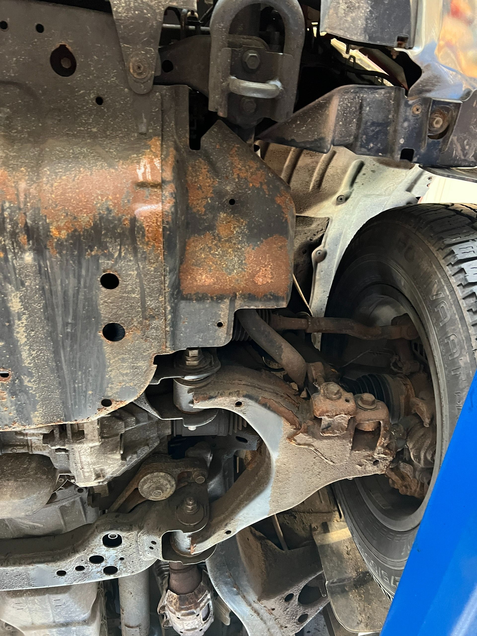 Rusty car undercarriage with suspension and wheel visible on a lift
