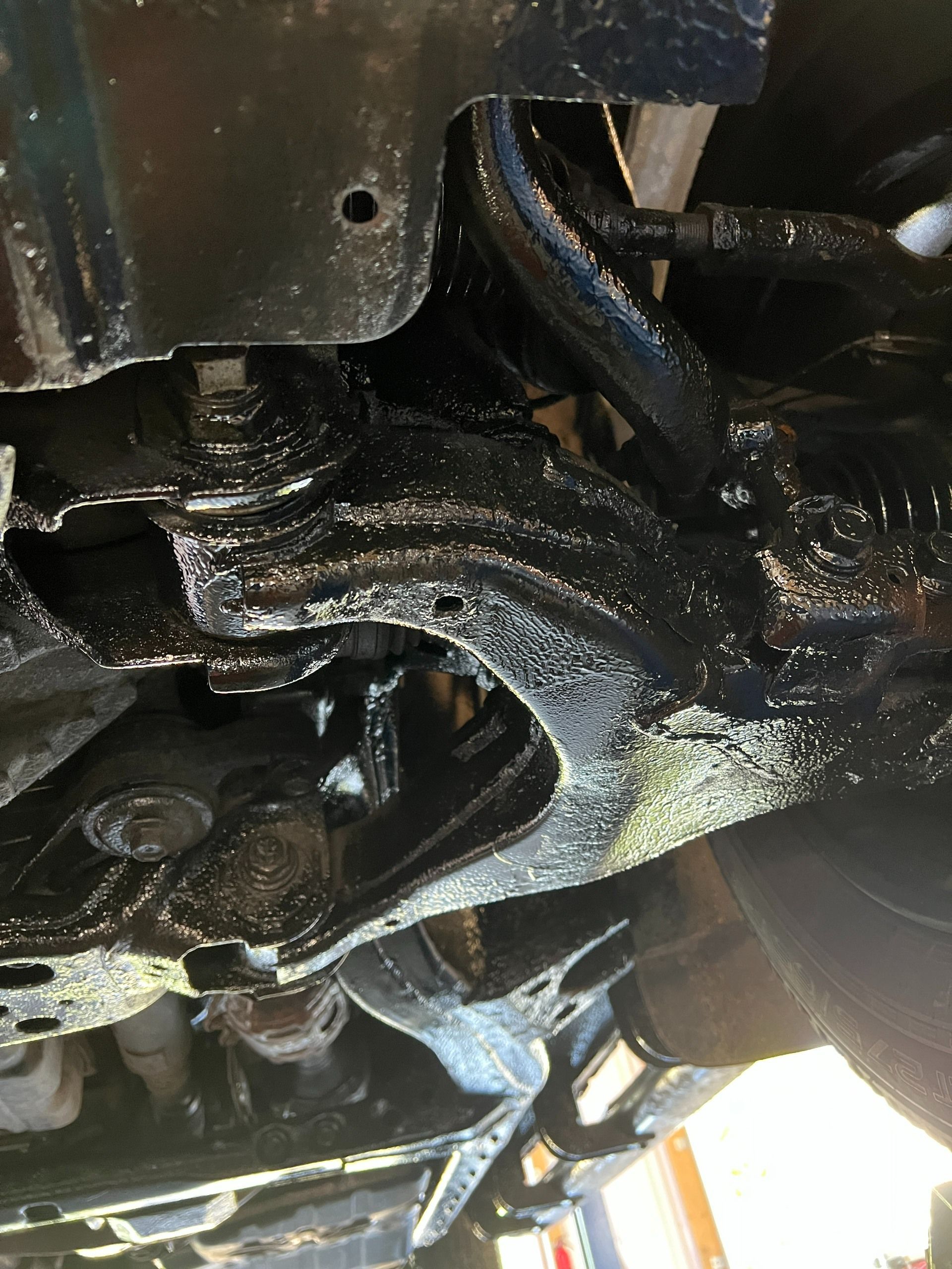 Close-up of a greasy black metal vehicle undercarriage with a suspension bracket and wiring visible