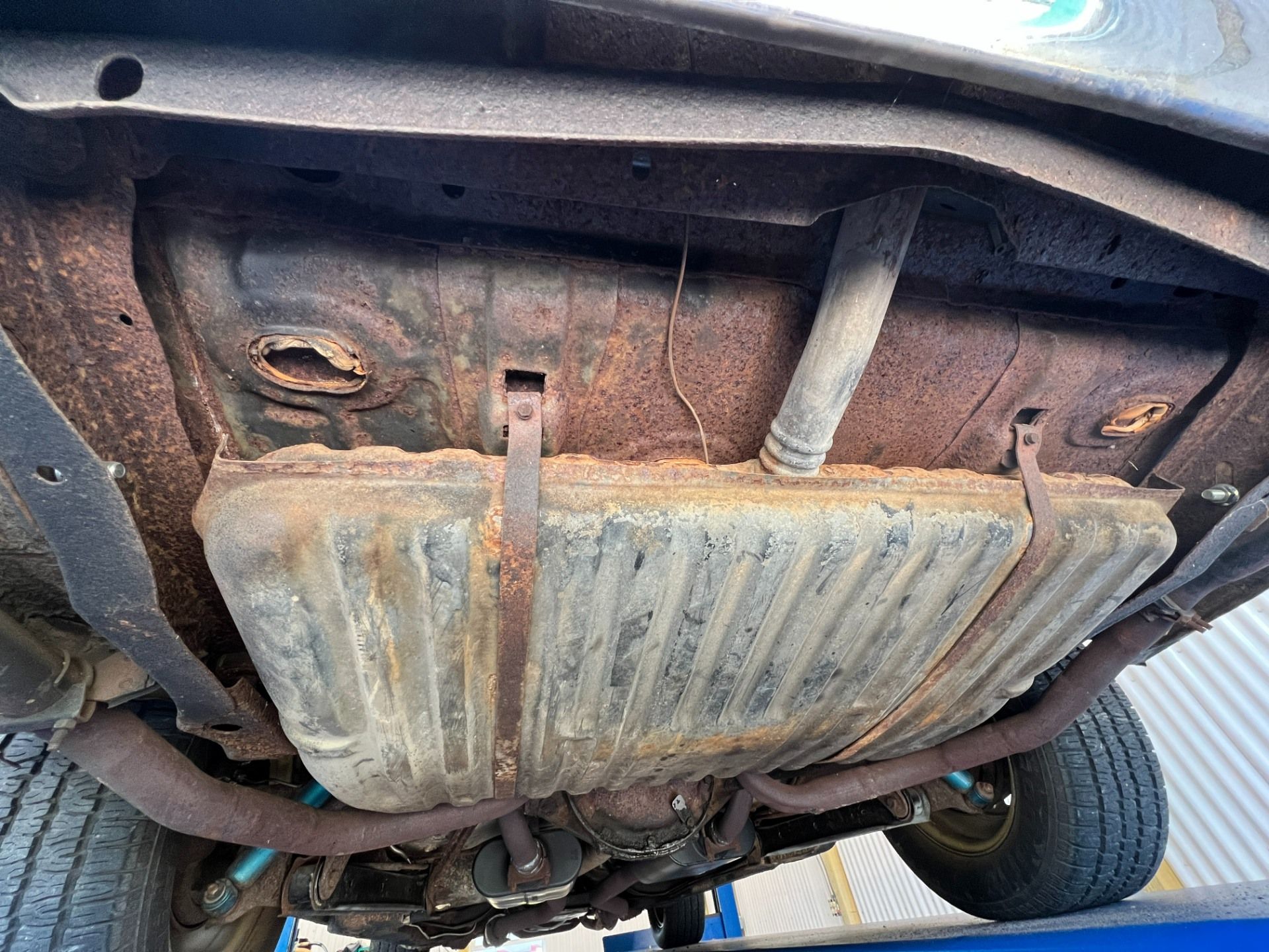 Rusty car undercarriage with fuel tank and suspension visible on a lift