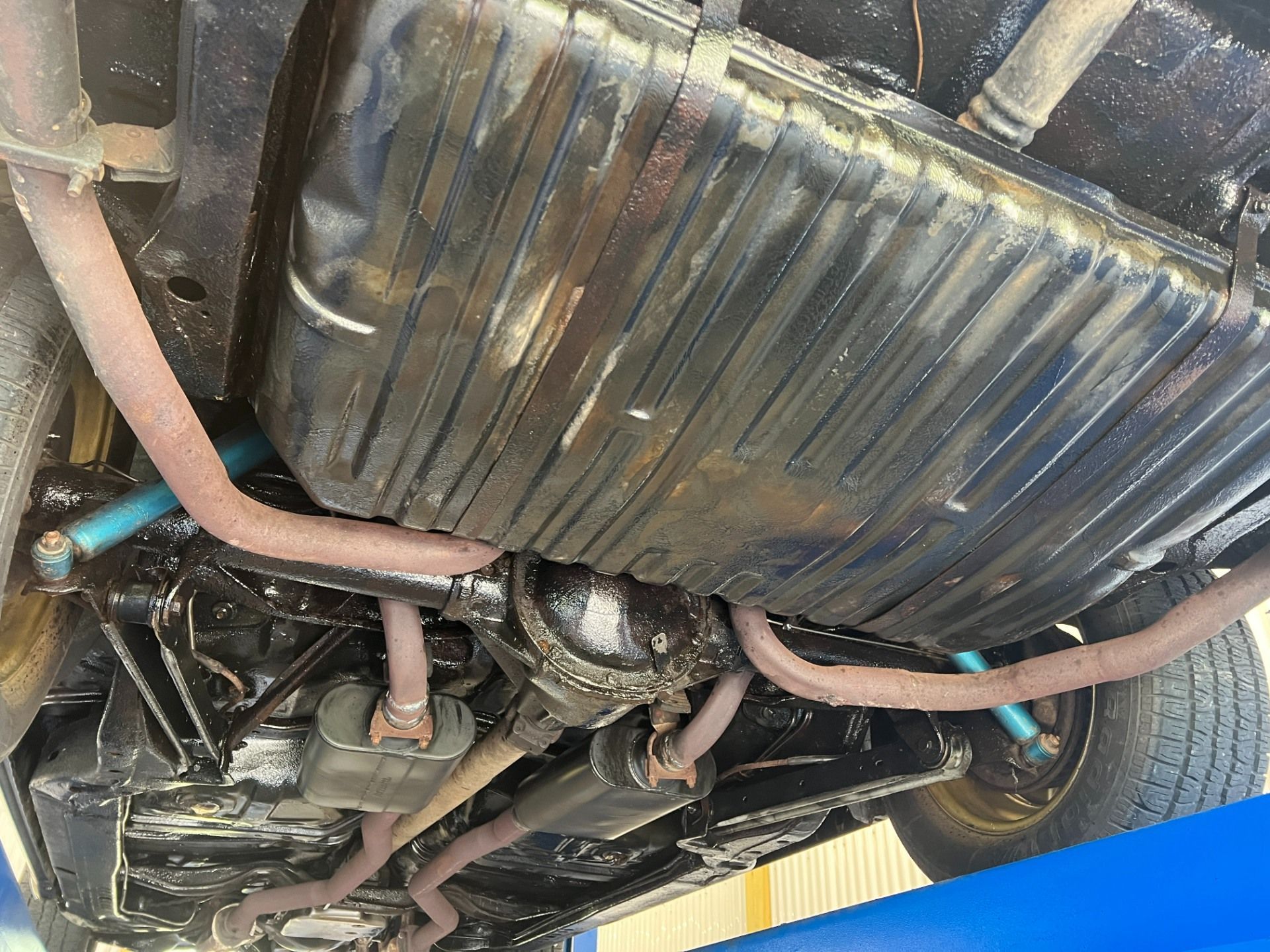Underside of a car showing the exhaust, fuel tank, and suspension near a rear wheel.