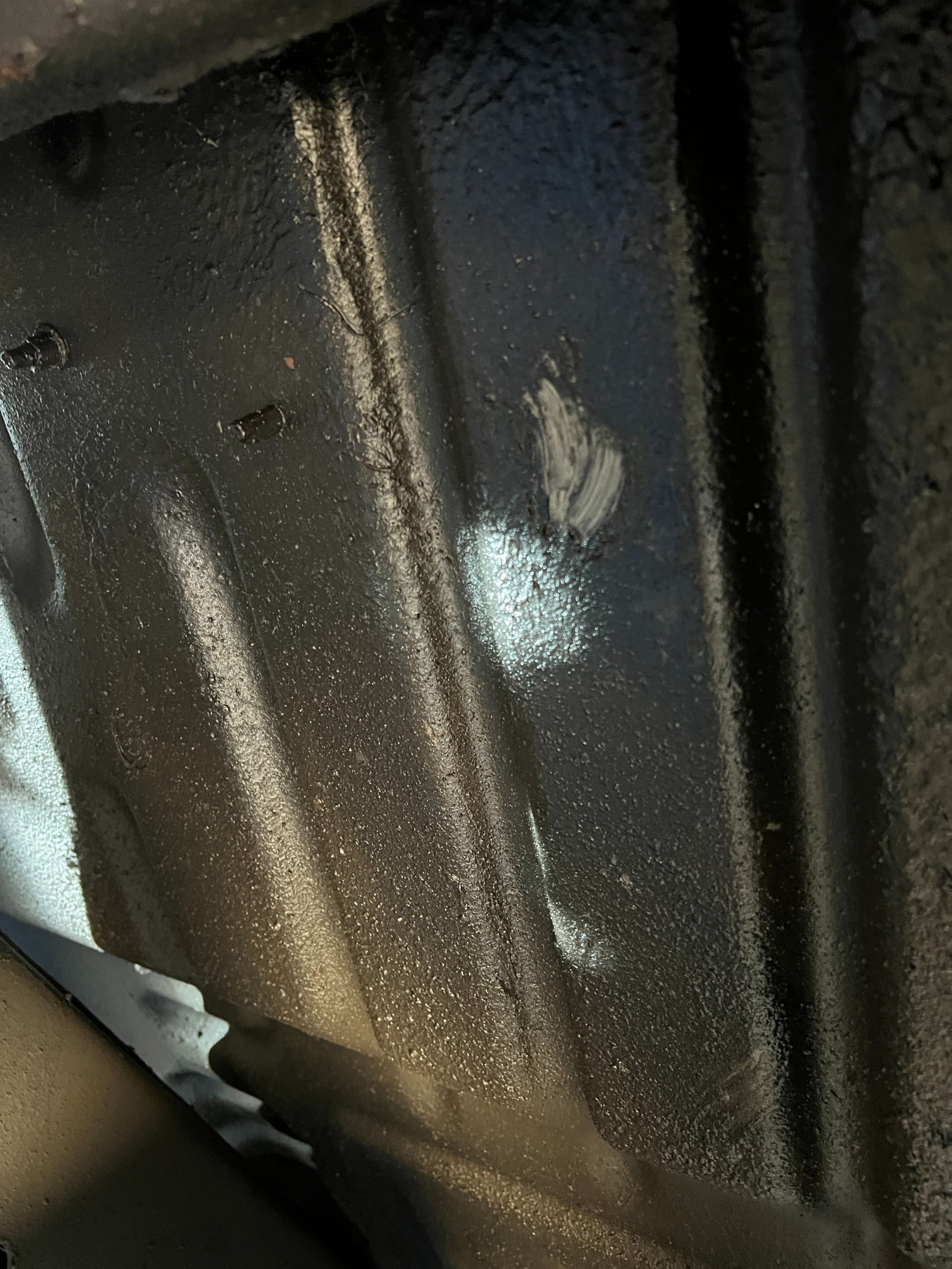 Close-up of a dark metal surface with a small white patch and water droplets