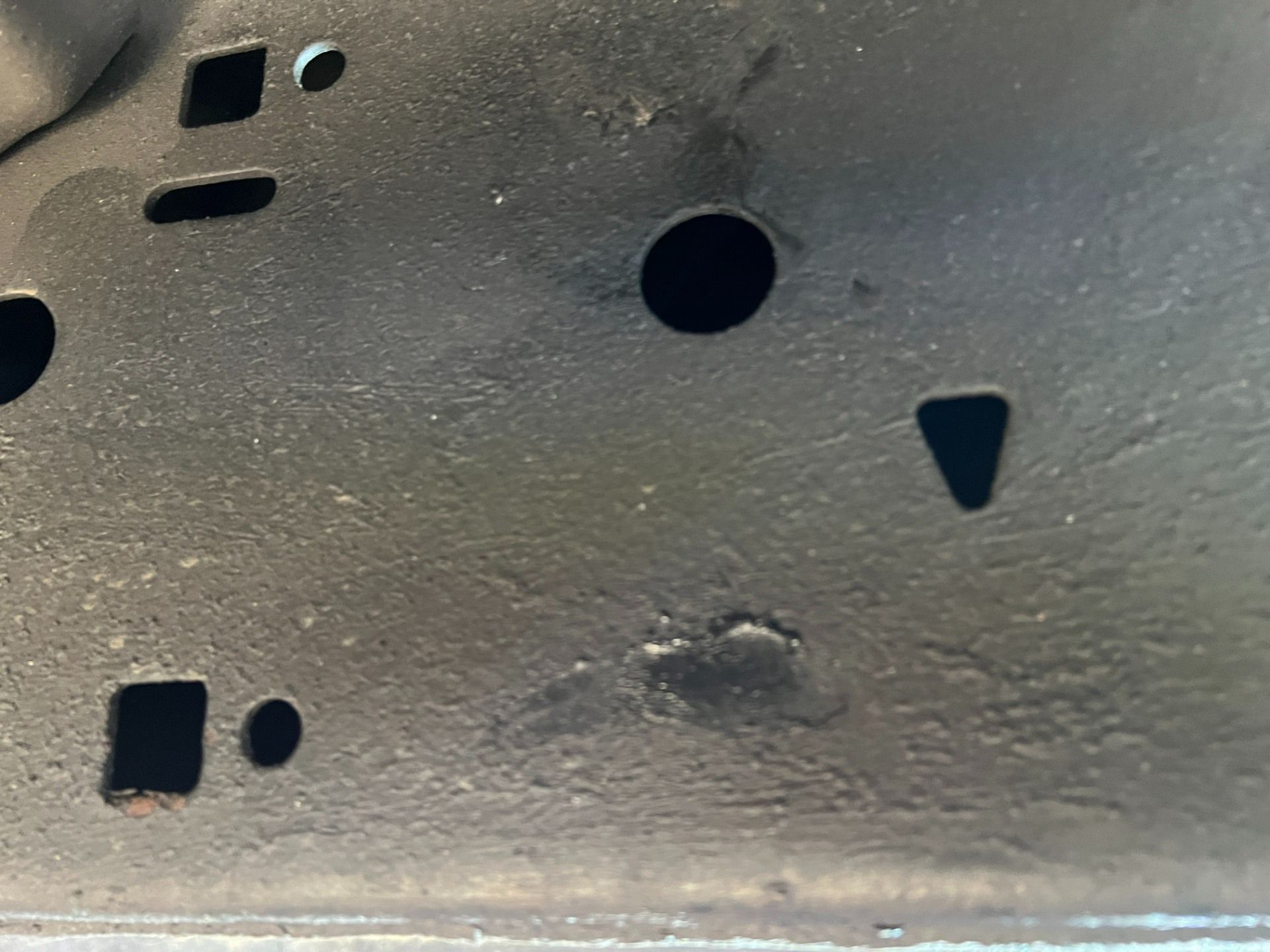 Close-up of a dark gray metal surface with various holes and cutouts, including a small dent or smudge near the bottom.