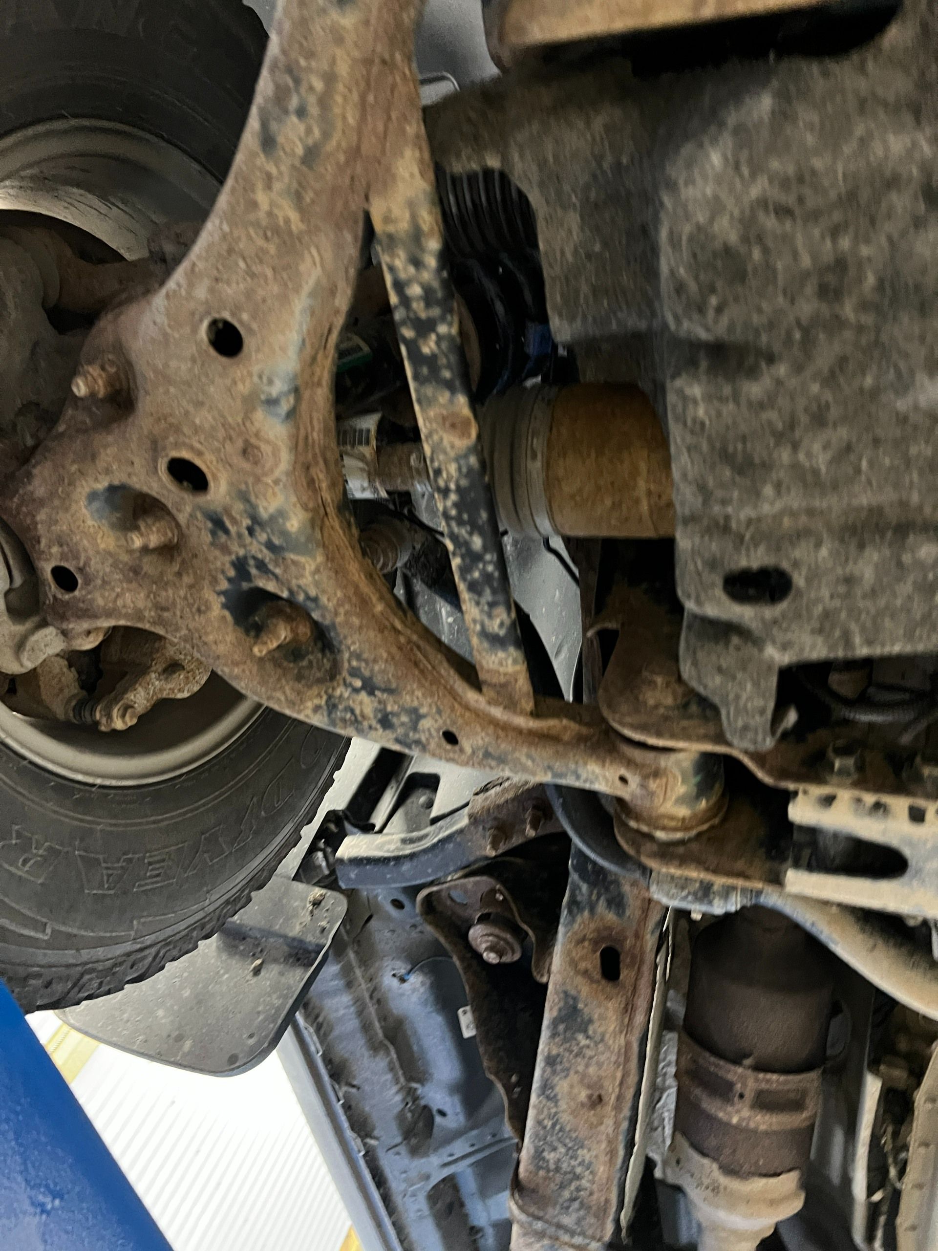 Undercarriage of a vehicle, showing rusted suspension and steering components near a wheel