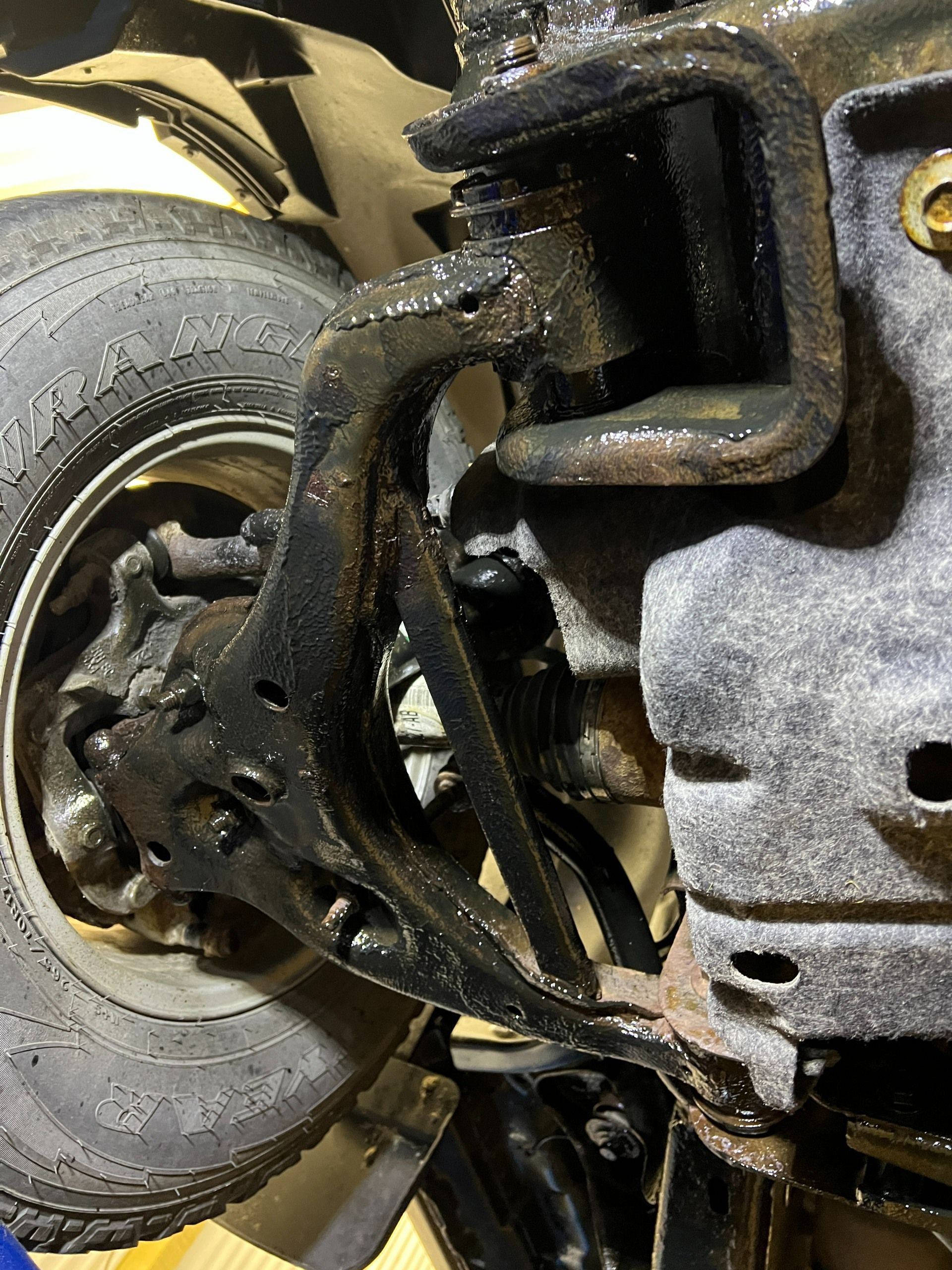 Close-up of a damaged wheel and suspension under a vehicle, showing bent metal parts and tire wear