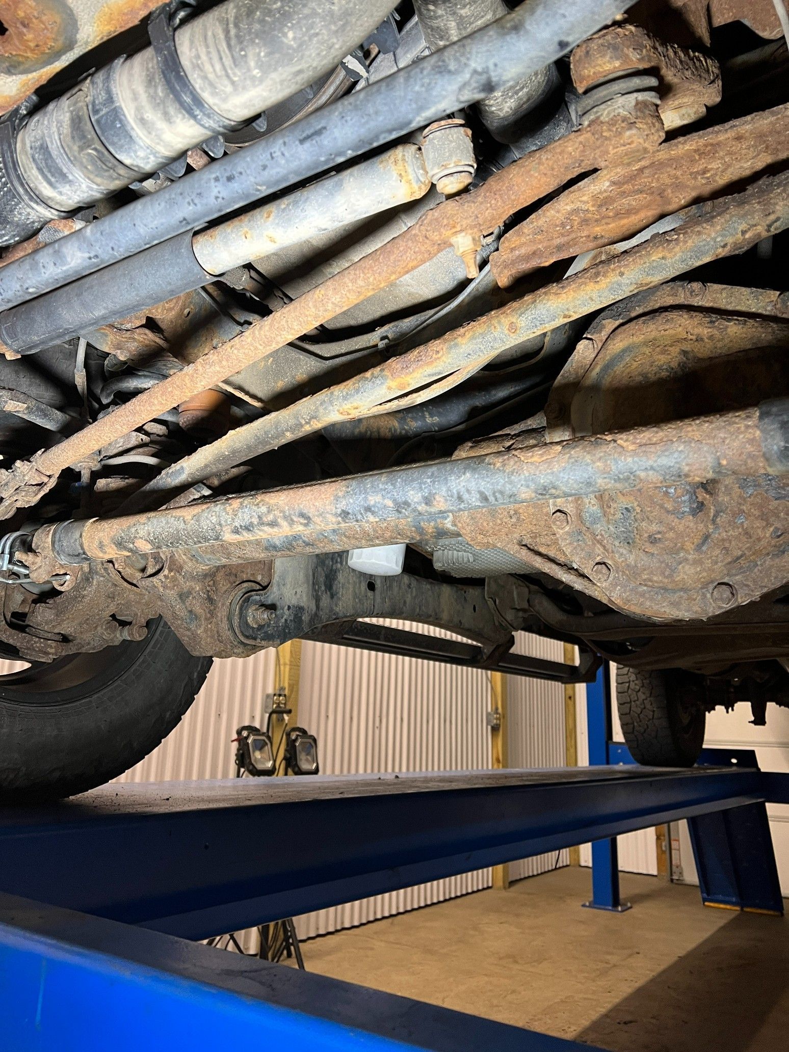 Rusty underside of a vehicle on a lift, with suspension and exhaust components visible