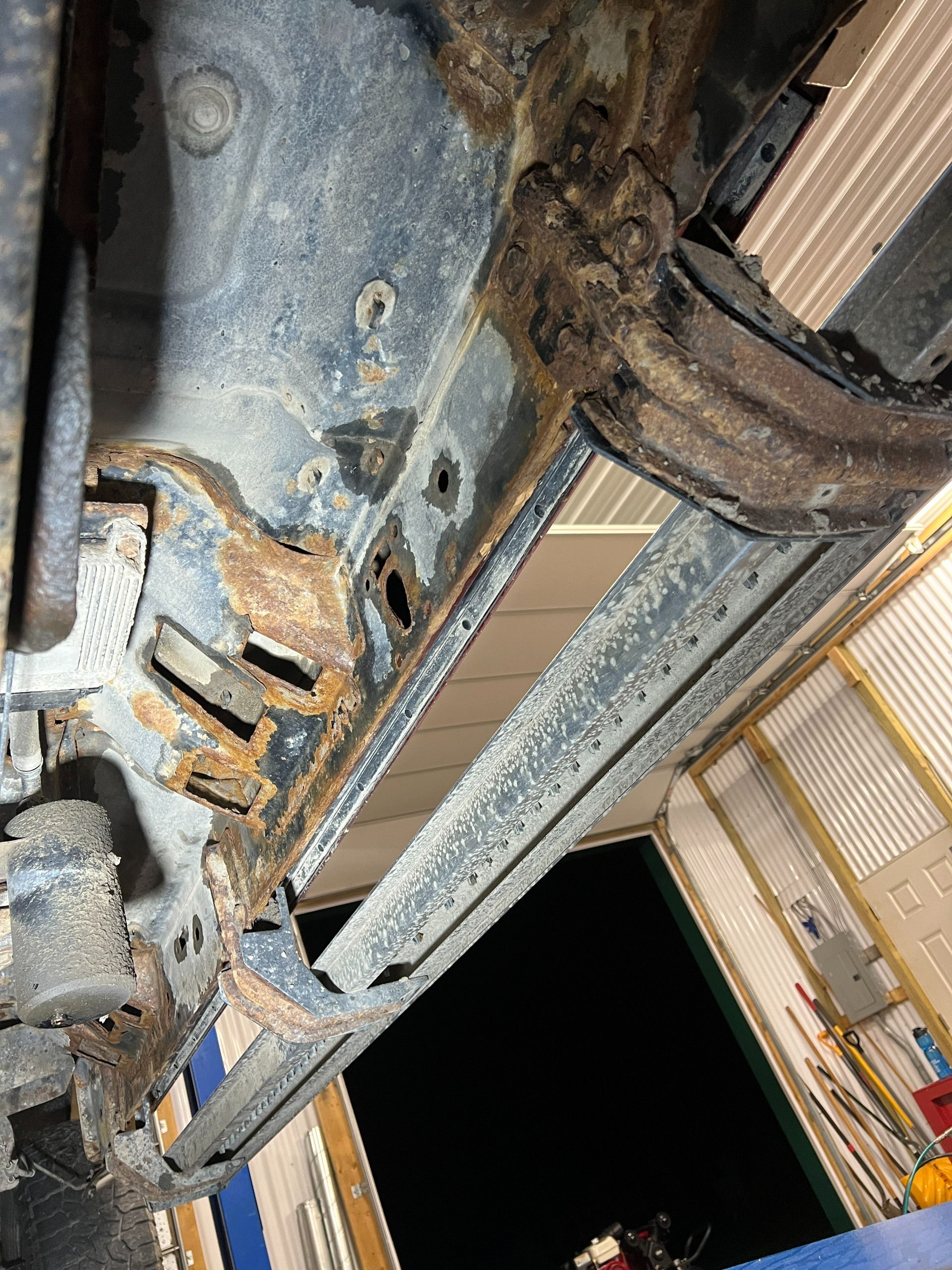 Rusty metal machinery underside with cables and beams inside an industrial structure, viewed at night