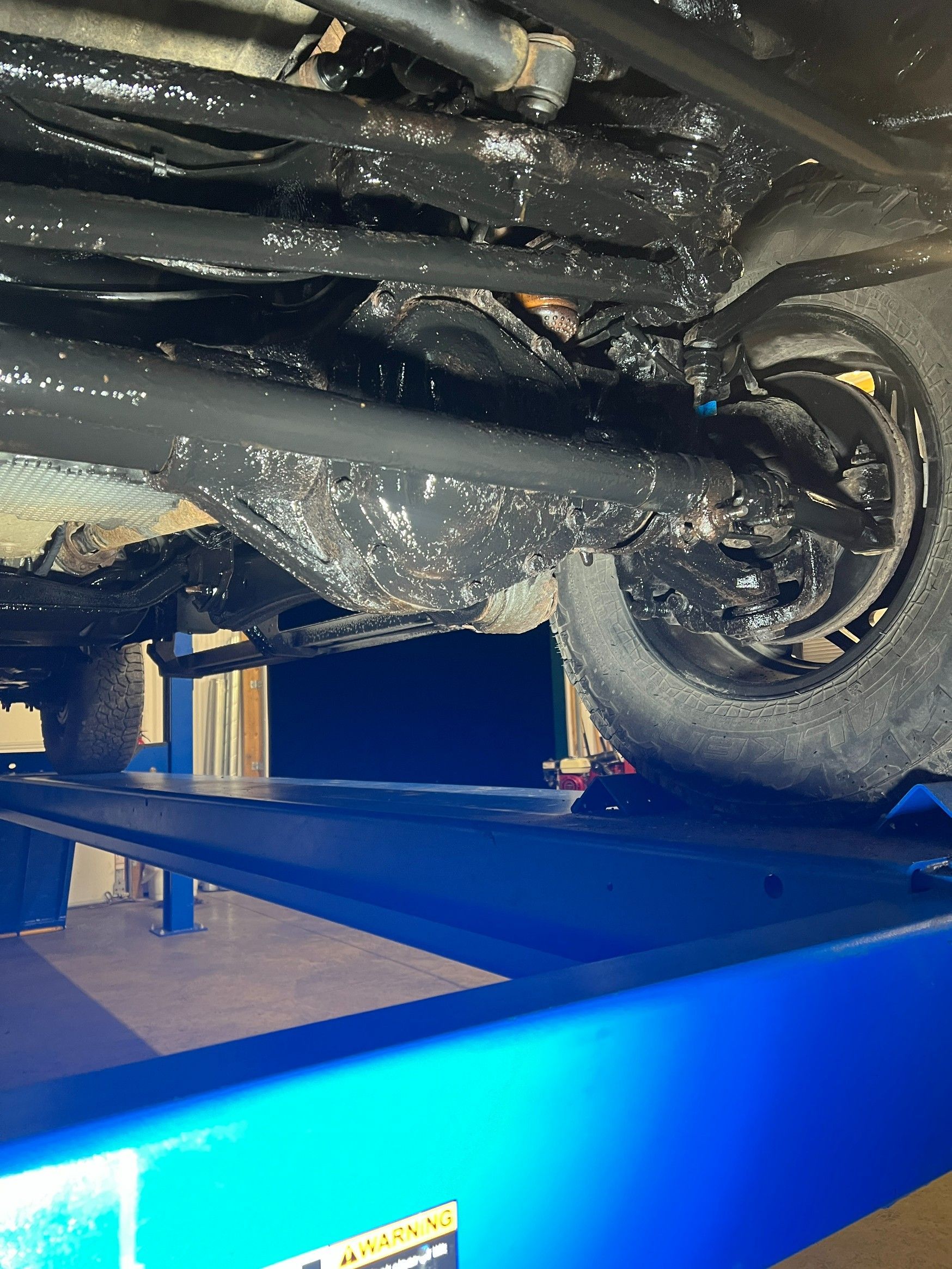 Undercarriage of a vehicle on a blue lift in a garage, showing suspension and wheel area.