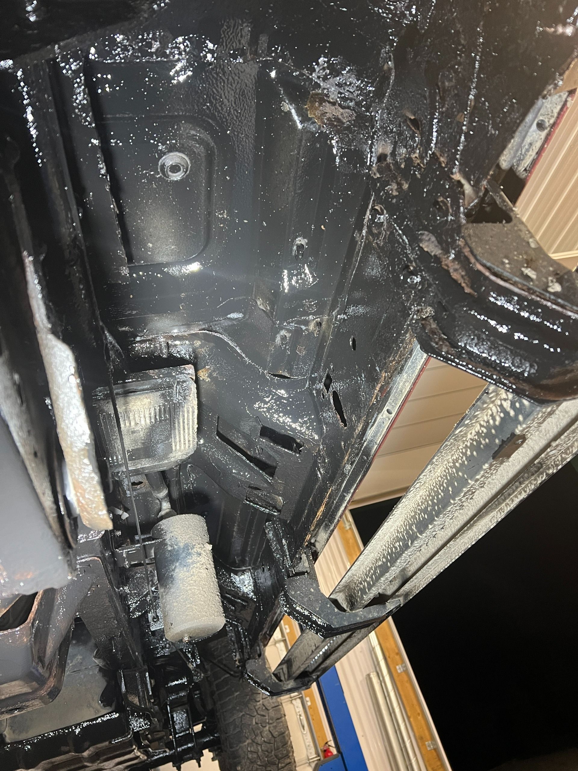 Close-up of a black car undercarriage with wet, muddy surfaces and visible suspension parts
