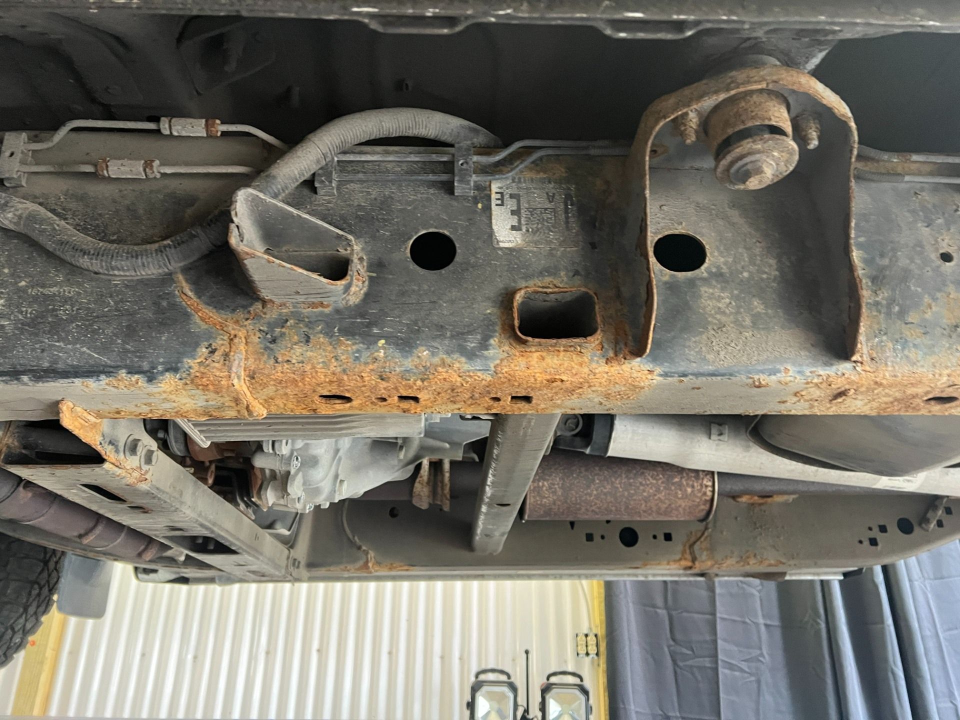 Undercarriage of a vehicle with rusted metal frame and suspension parts visible at a repair shop lift