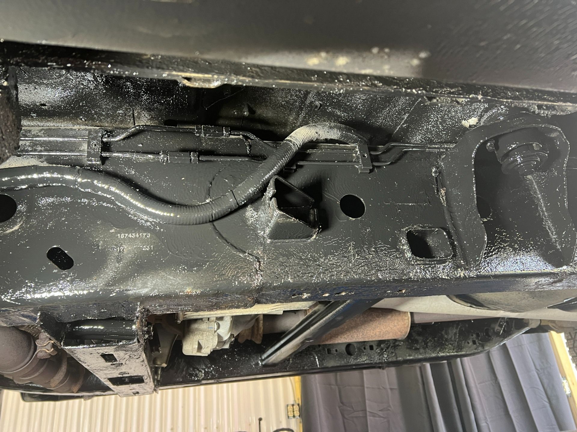 Undercarriage of a car with a black, wet metal frame and visible exhaust and suspension parts