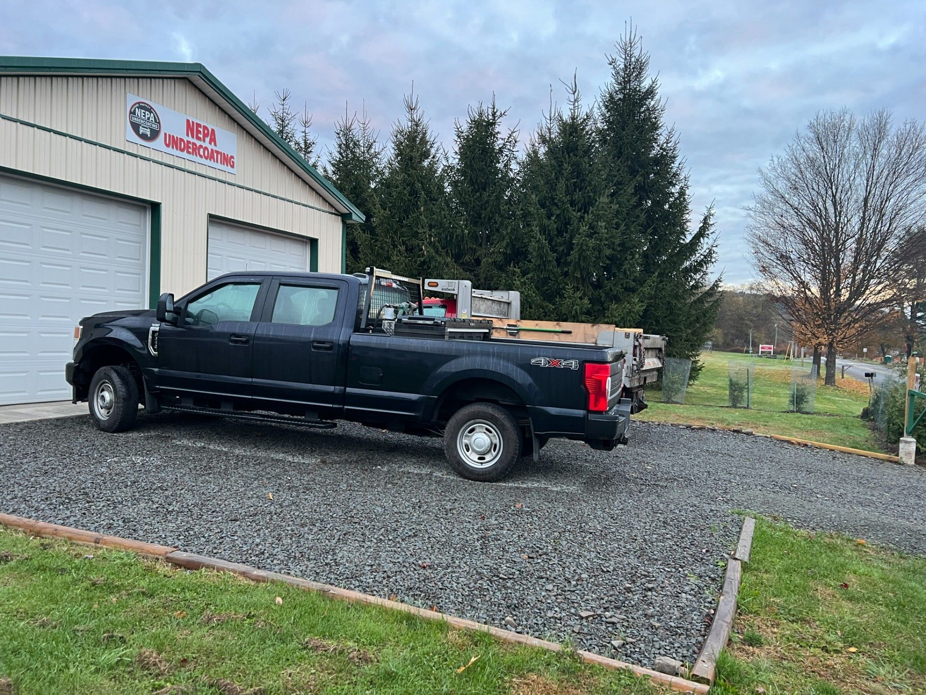 Black pickup truck parked on a gravel driveway beside a white garage with trees and a grassy yard.