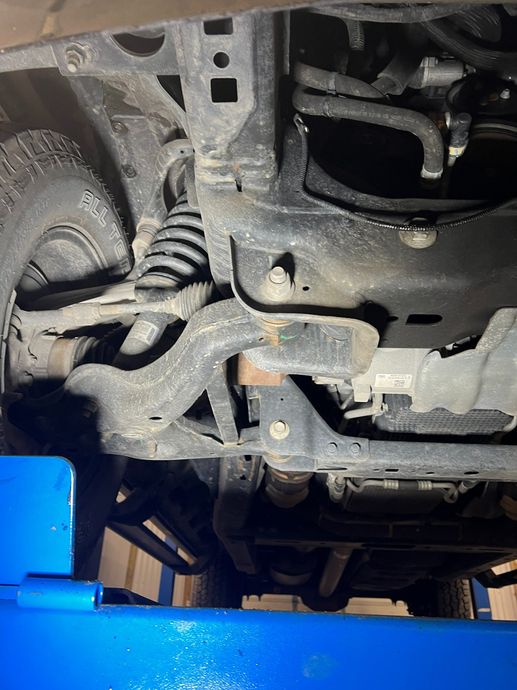 Undercarriage of a vehicle on a blue lift, showing suspension and exhaust components.