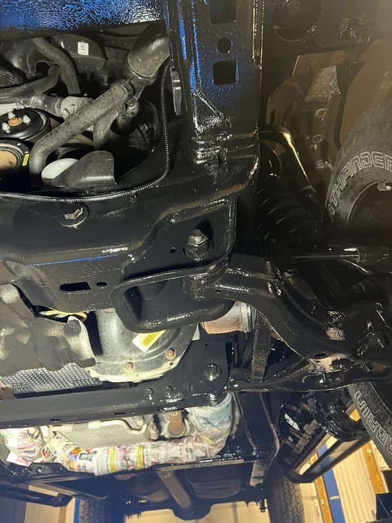 Close-up of wet vehicle undercarriage with engine parts and hoses, likely in a repair shop
