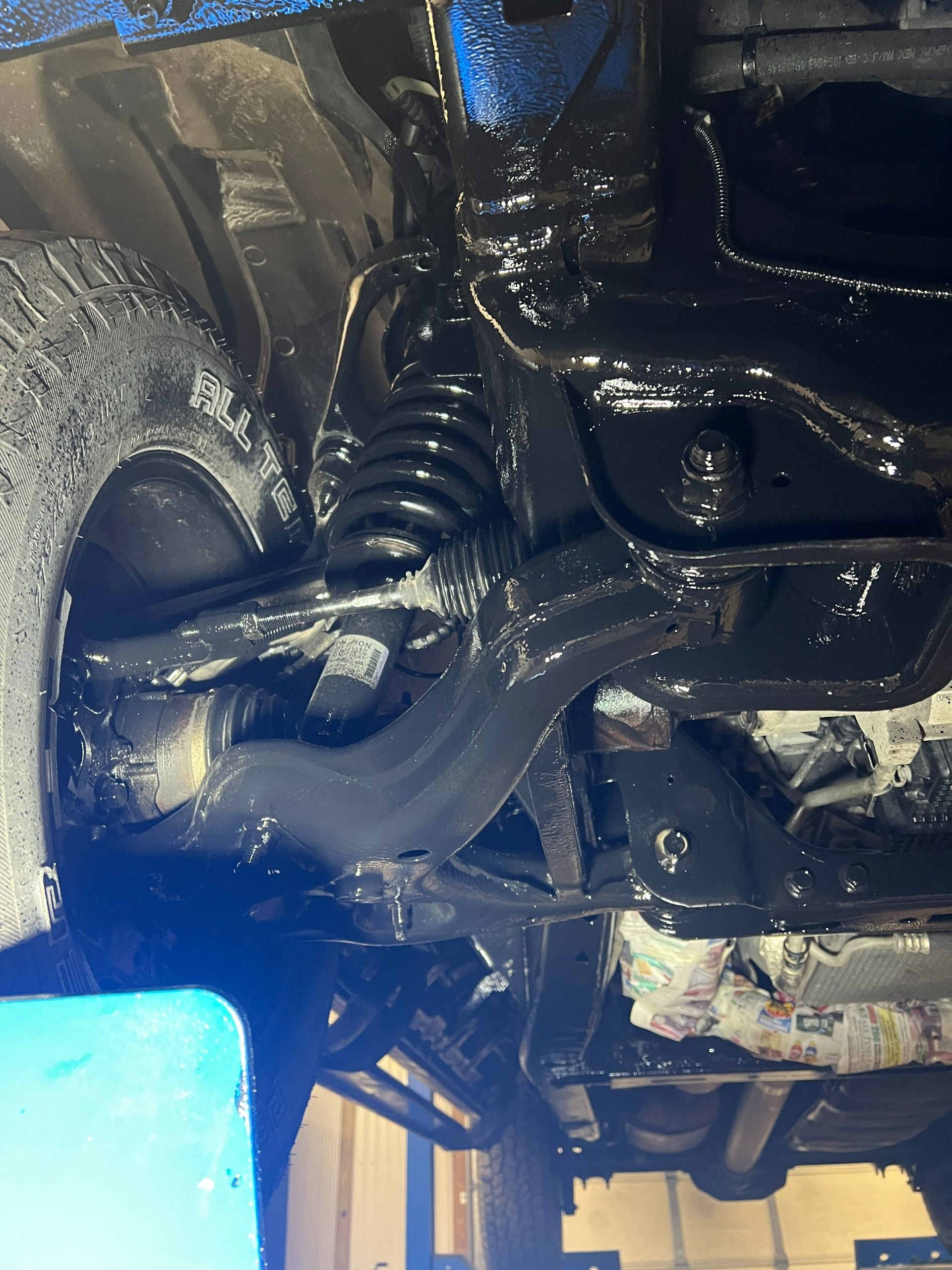 Close-up of a wet black mechanical assembly with hoses and a spring under bright blue light