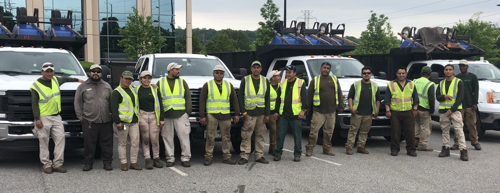 A group of construction workers are posing for a picture in front of their trucks.
