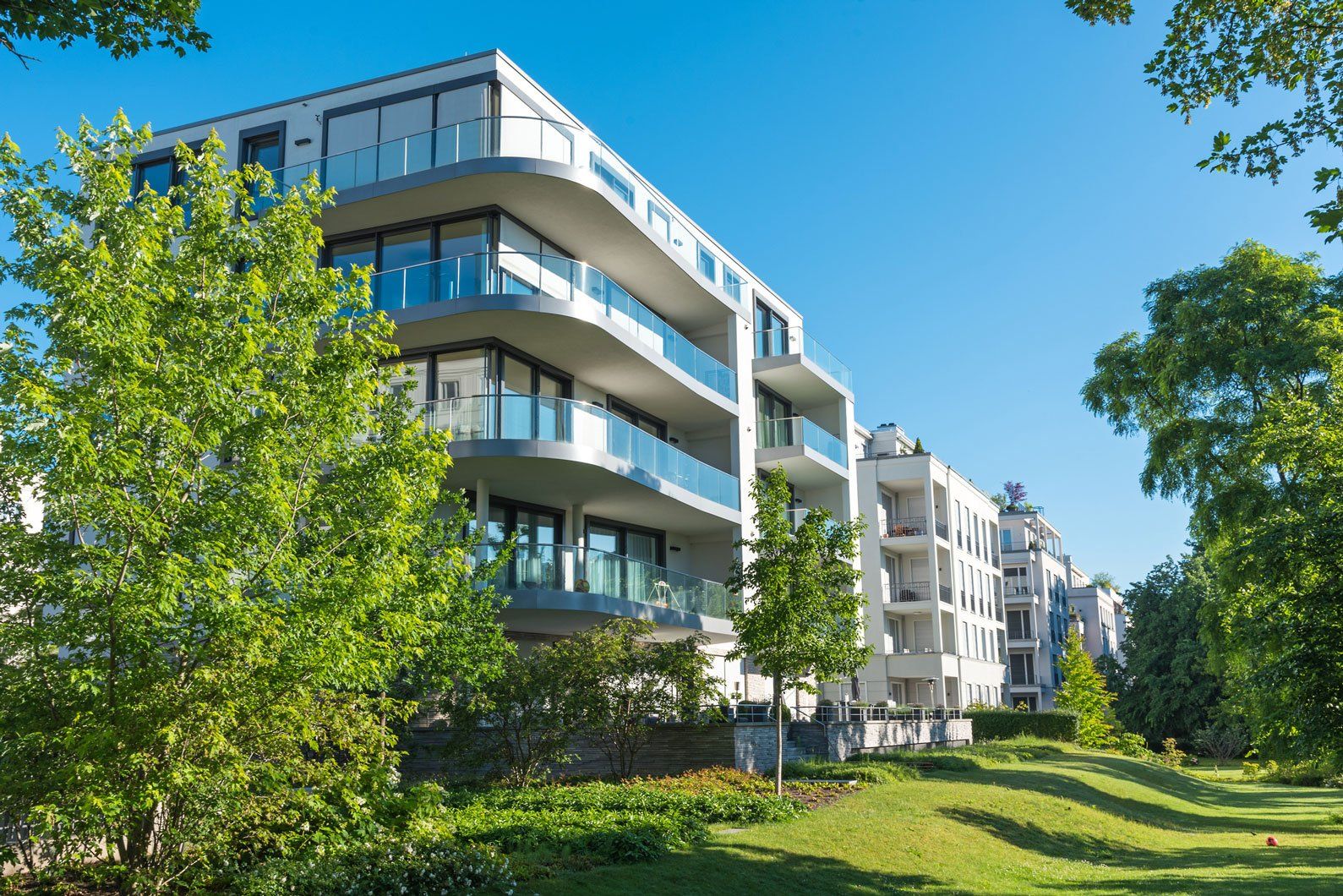 A large apartment building with a lot of windows is surrounded by trees and grass.