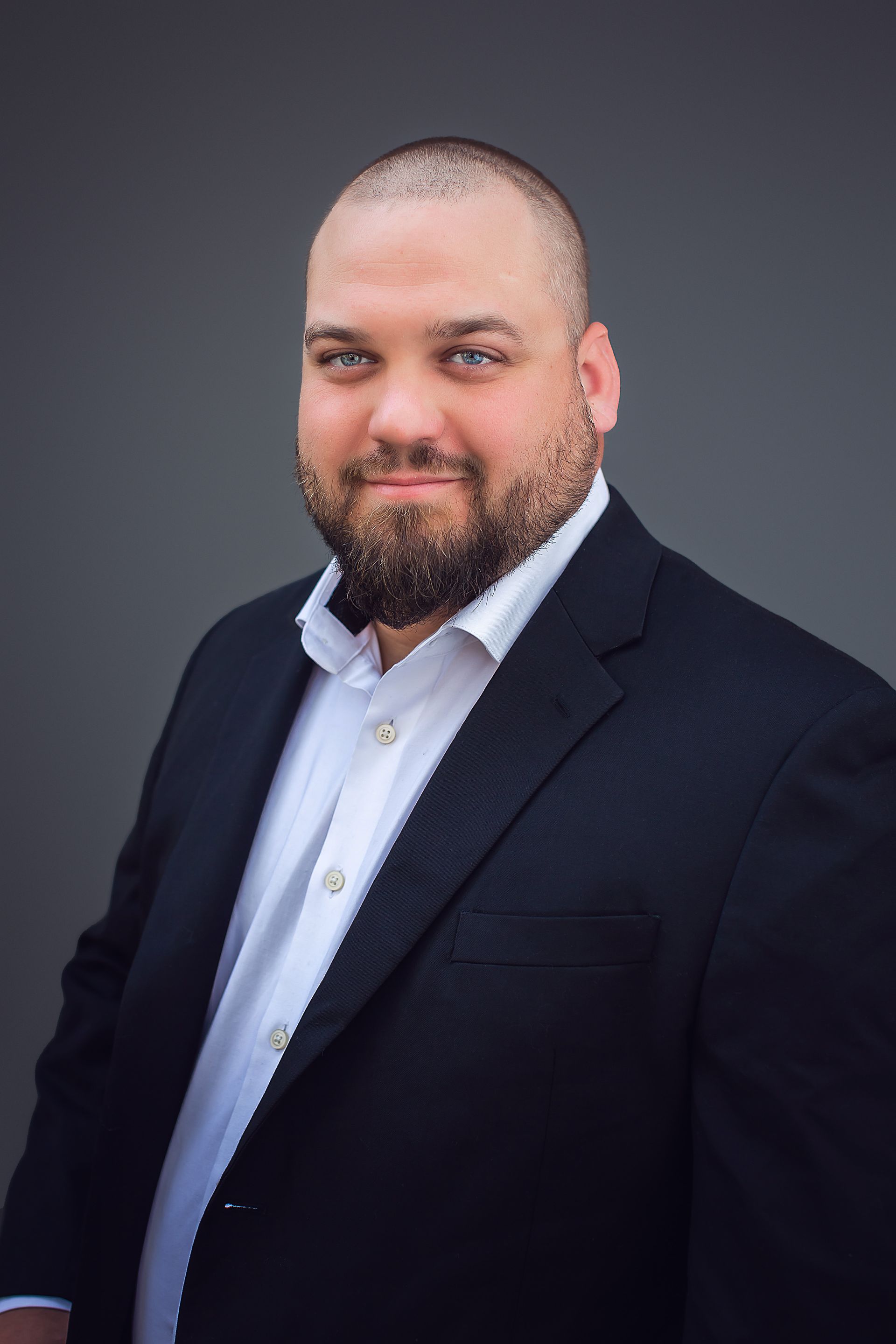 A man with a beard is wearing a suit and a white shirt.