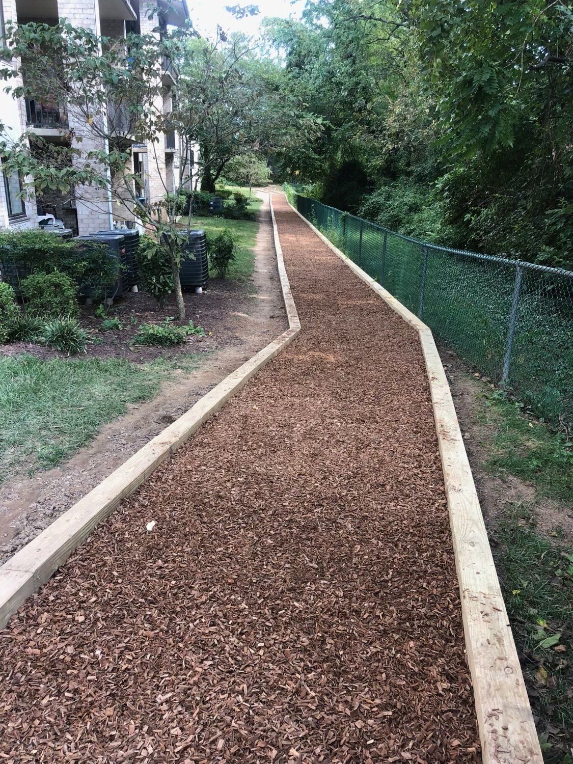A wooden walkway lined with brown mulch next to a chain link fence.