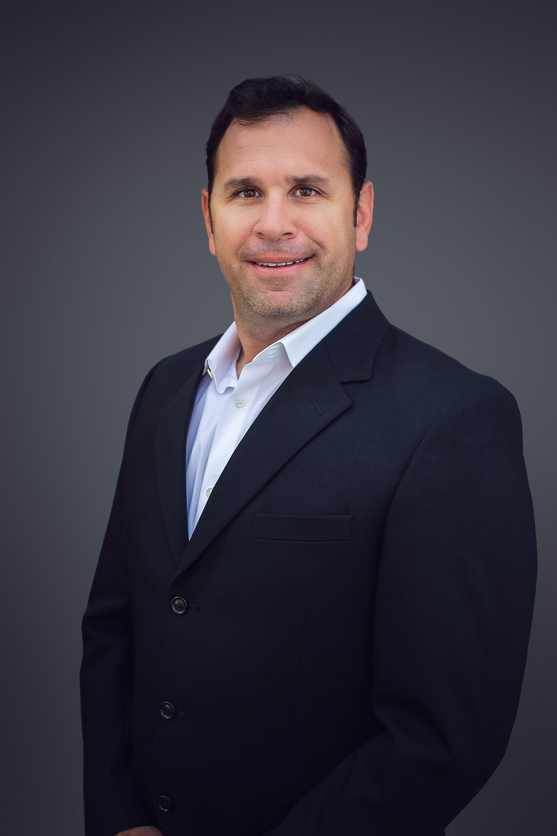 A man in a suit and white shirt is smiling for the camera.