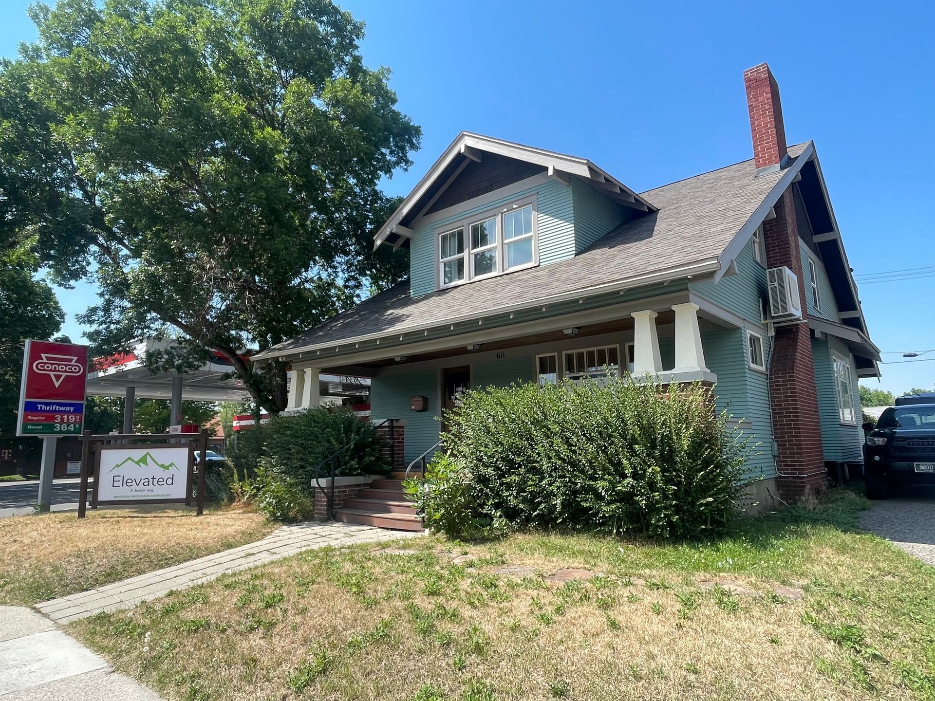 Blue house with green bushes, brick chimney, and business signs, sidewalk in front.