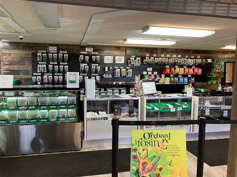Interior of a dispensary with display cases, shelves of products, and a sign for Orchard Tressin's.