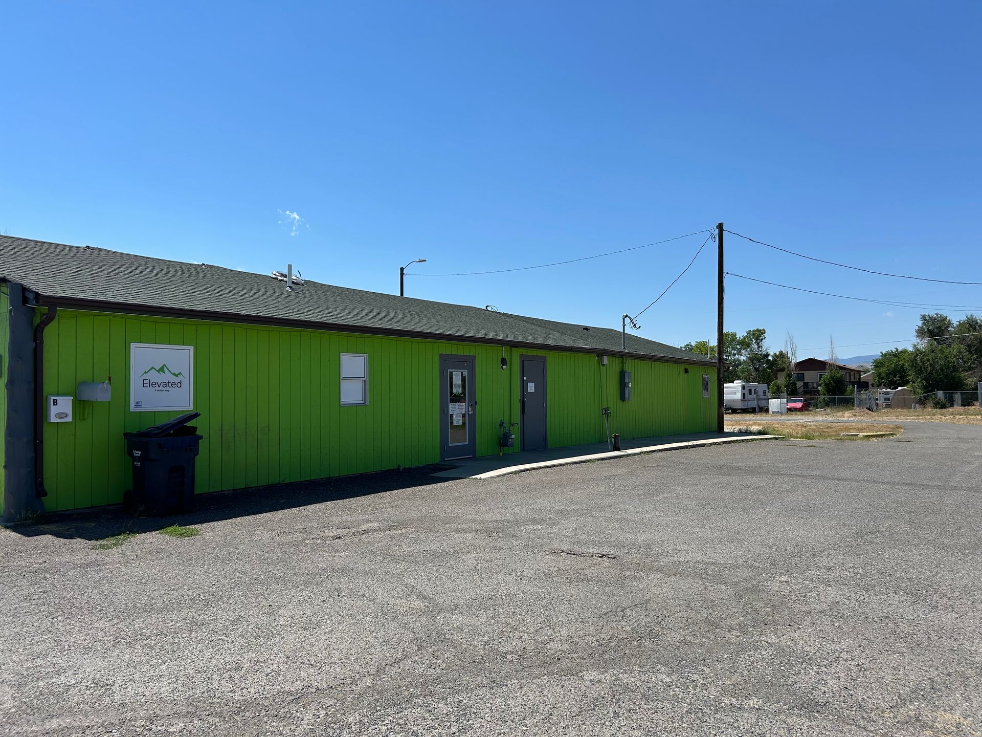 Bright green building with dark roof, gravel parking lot, clear blue sky.