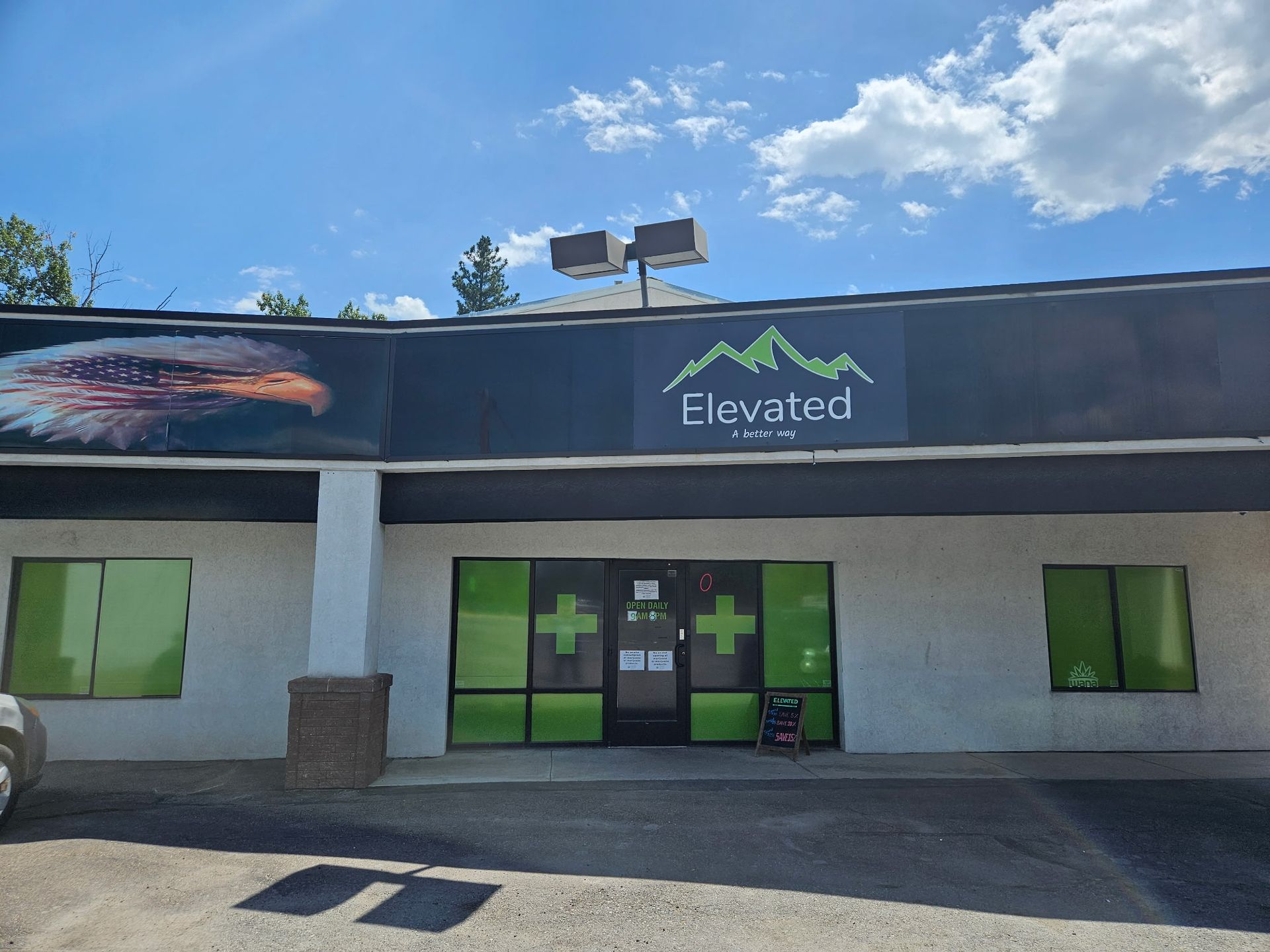 Elevated dispensary storefront with eagle mural, green accents, and cross logos.