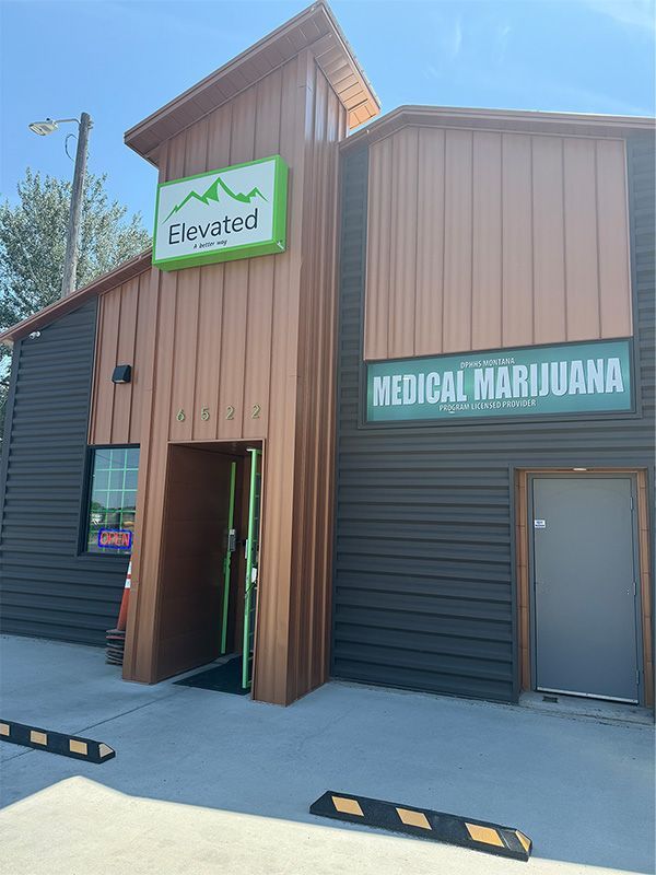 Elevated medical marijuana dispensary with green sign and open door. Brown and gray exterior.