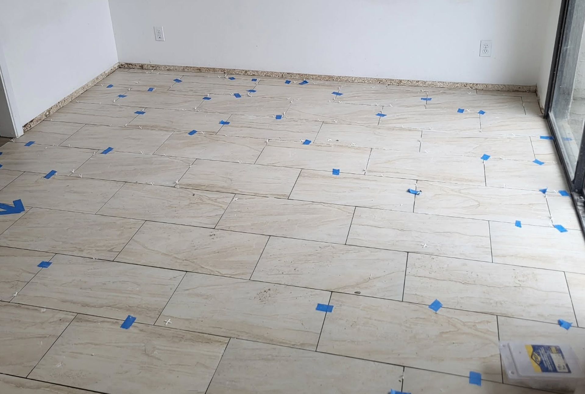 Floor tiles laid out with blue tape spacers. Room under construction.