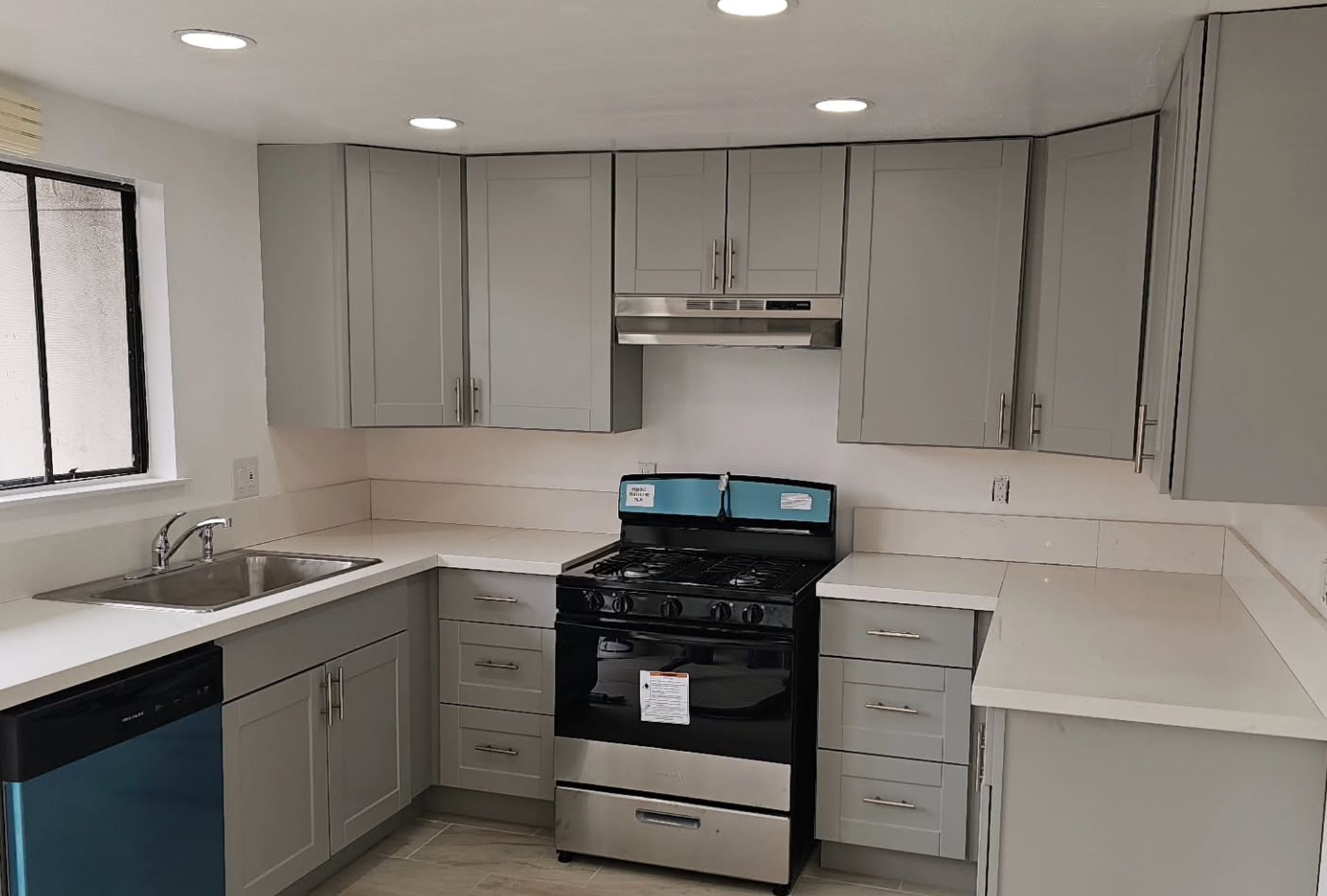Gray kitchen cabinets with white countertops, a stove, and stainless steel appliances.