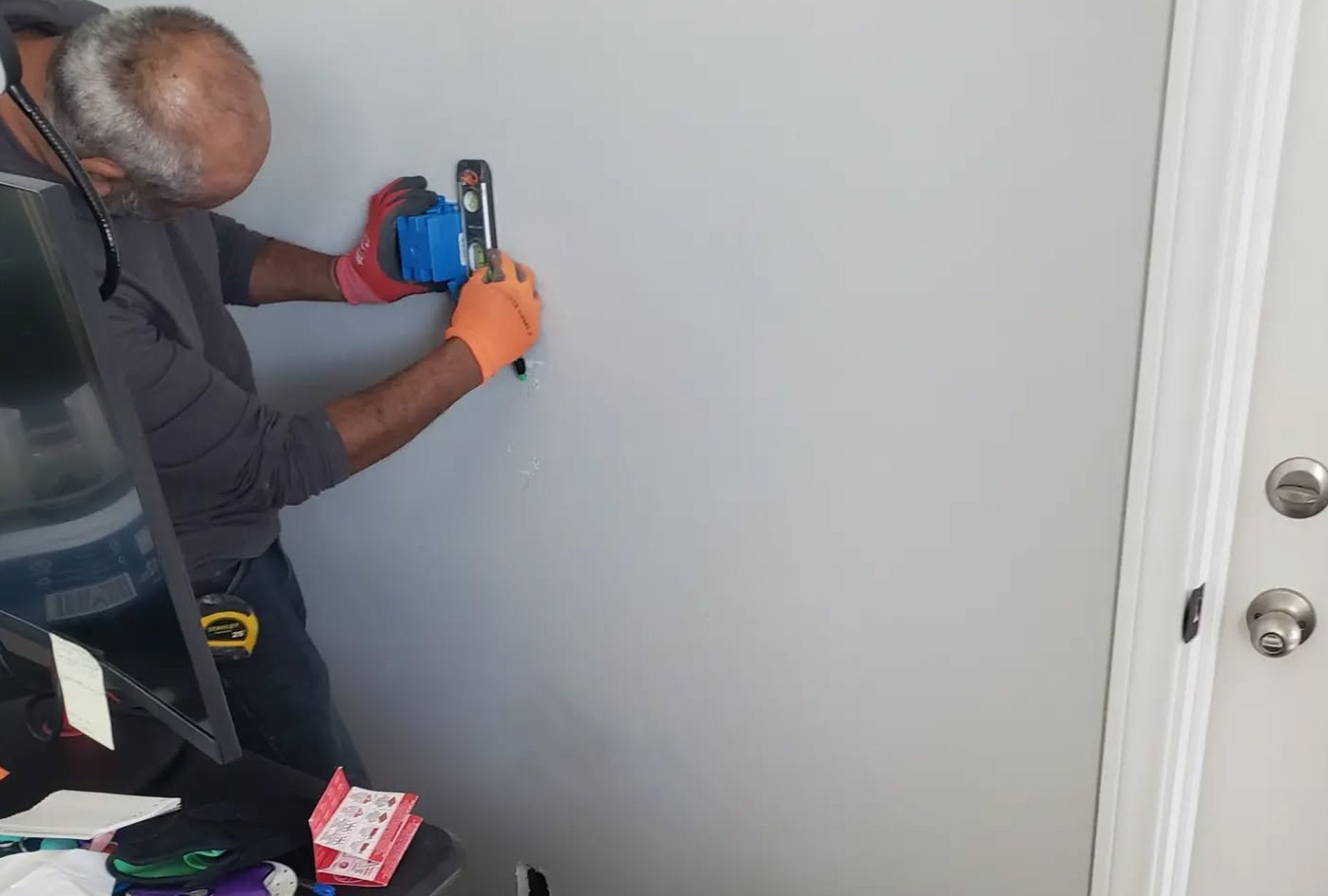 Person installing an electrical outlet on a gray wall. They are wearing gloves and using tools.