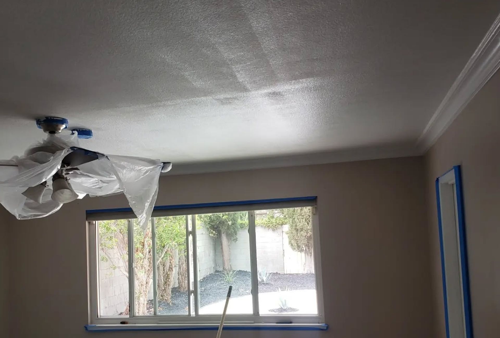 Room interior with partially painted ceiling, window, and taped trim.