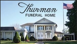 Thurman Funeral Home sign above a white colonial-style building with an American flag flying outside