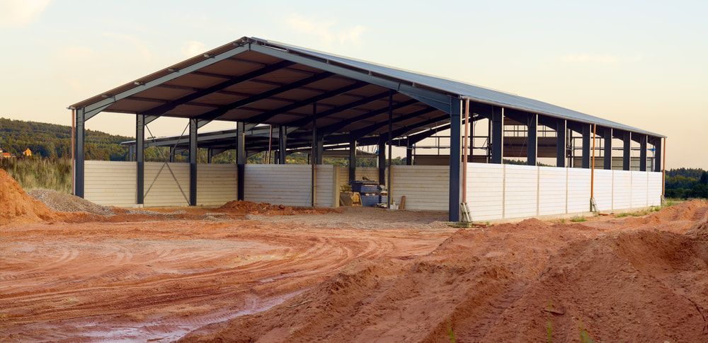 A Large Metal Building Is Being Built In A Dirt Field — Lonnie Henderson Concreting In Dubbo, NSW