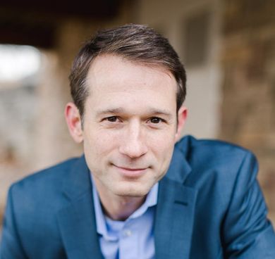 Man in a blue blazer and shirt smiling, outdoors.