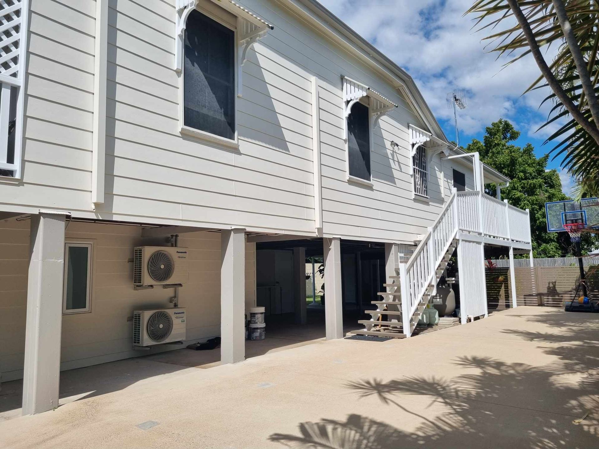 White wooden house on stilts with air conditioning units and a staircase.