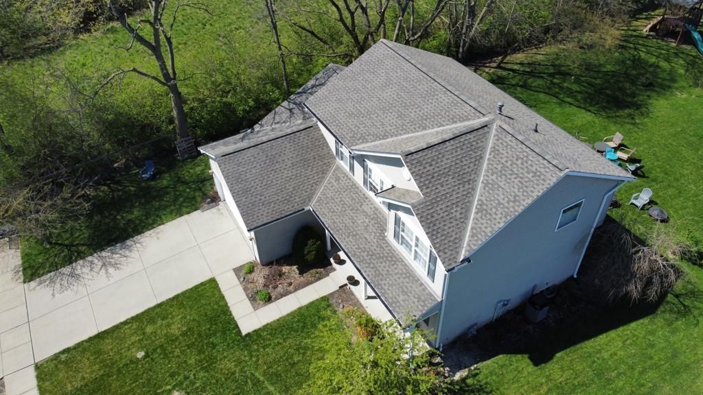 Aerial view of a gray-roofed house with a white driveway and green yard.