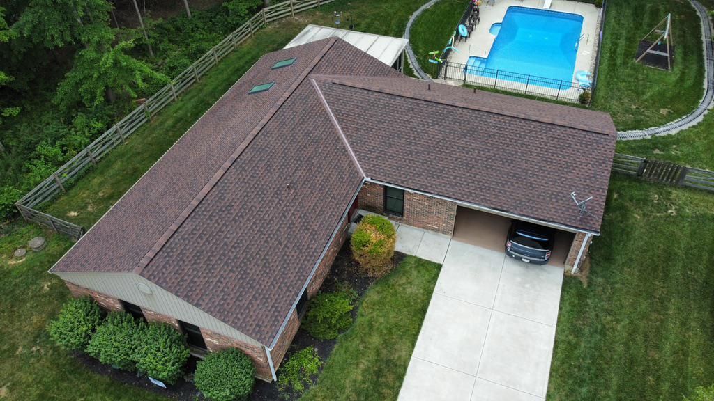 Aerial view of a brown-roofed house with a driveway and a backyard swimming pool