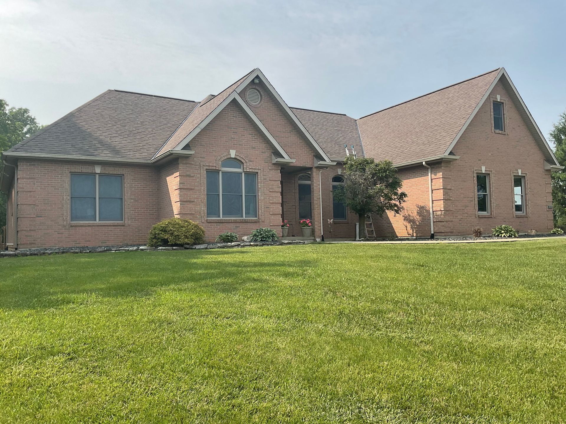 Brick suburban house with gray roof and green lawn under a cloudy sky