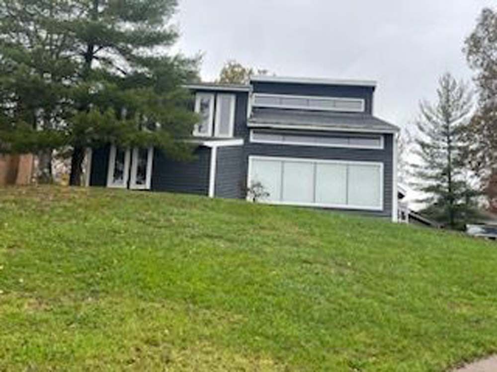 A large house is sitting on top of a lush green hill surrounded by trees.