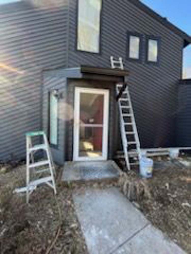 A ladder is sitting in front of a house that is being painted.