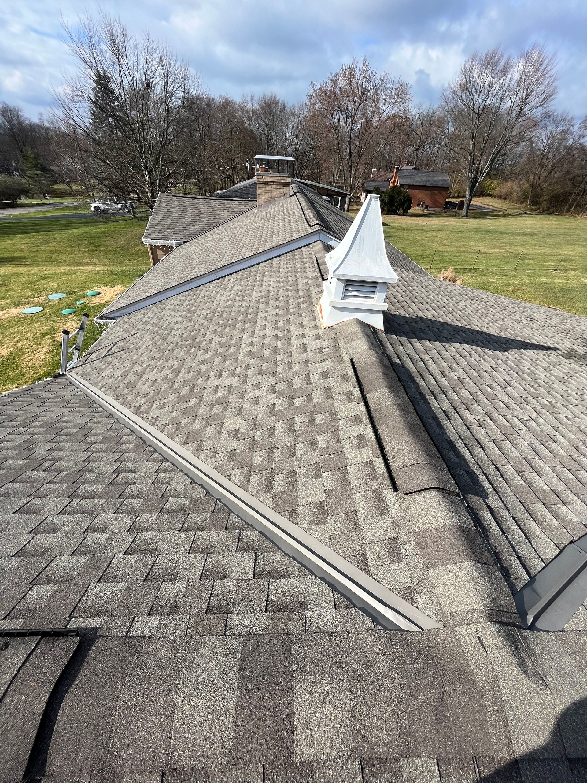 Gray shingled roof with a central white vent, viewed from above on a sunny day