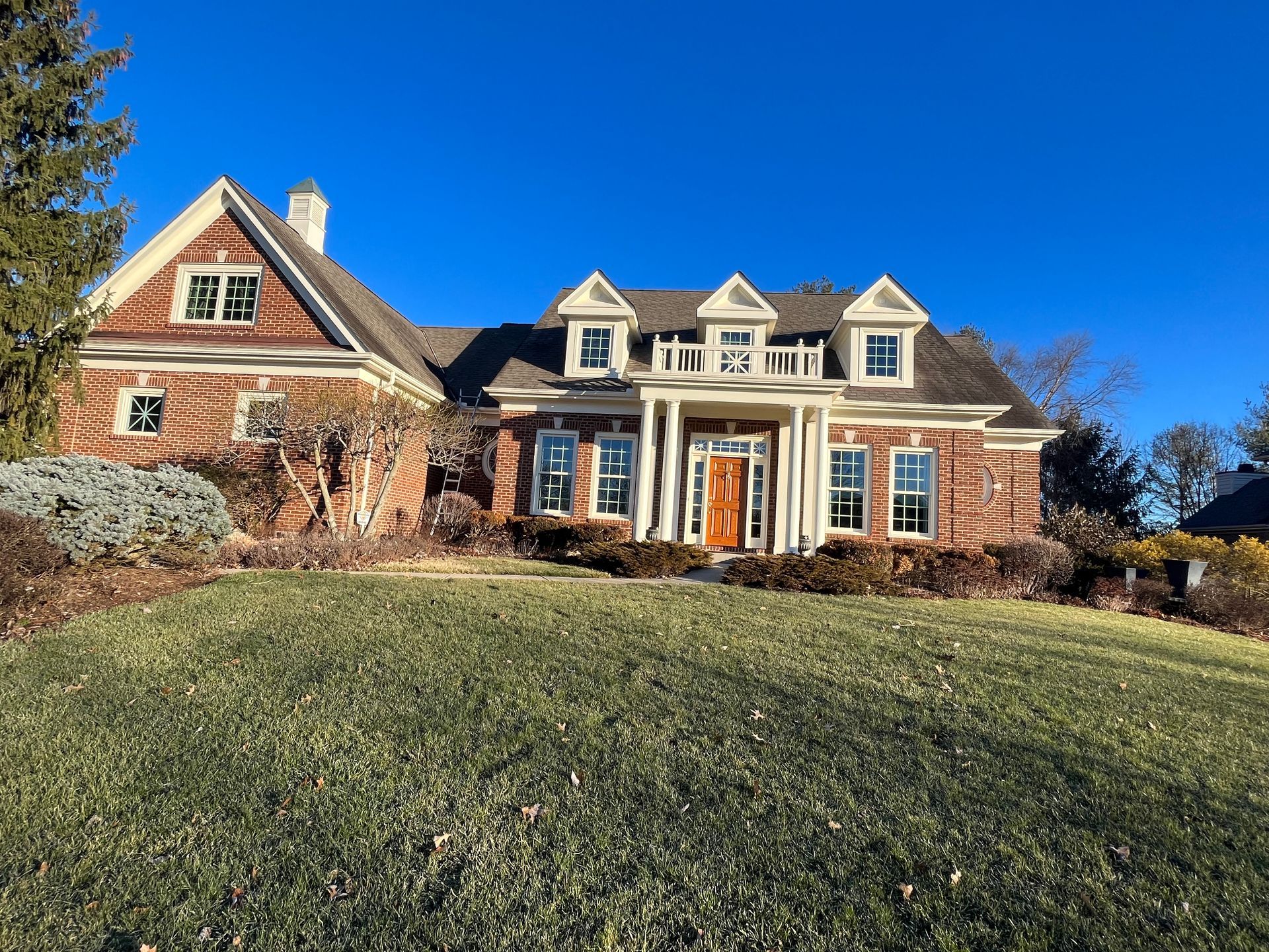 Large brick and shingle house with dormer windows on a grassy hill under a blue sky