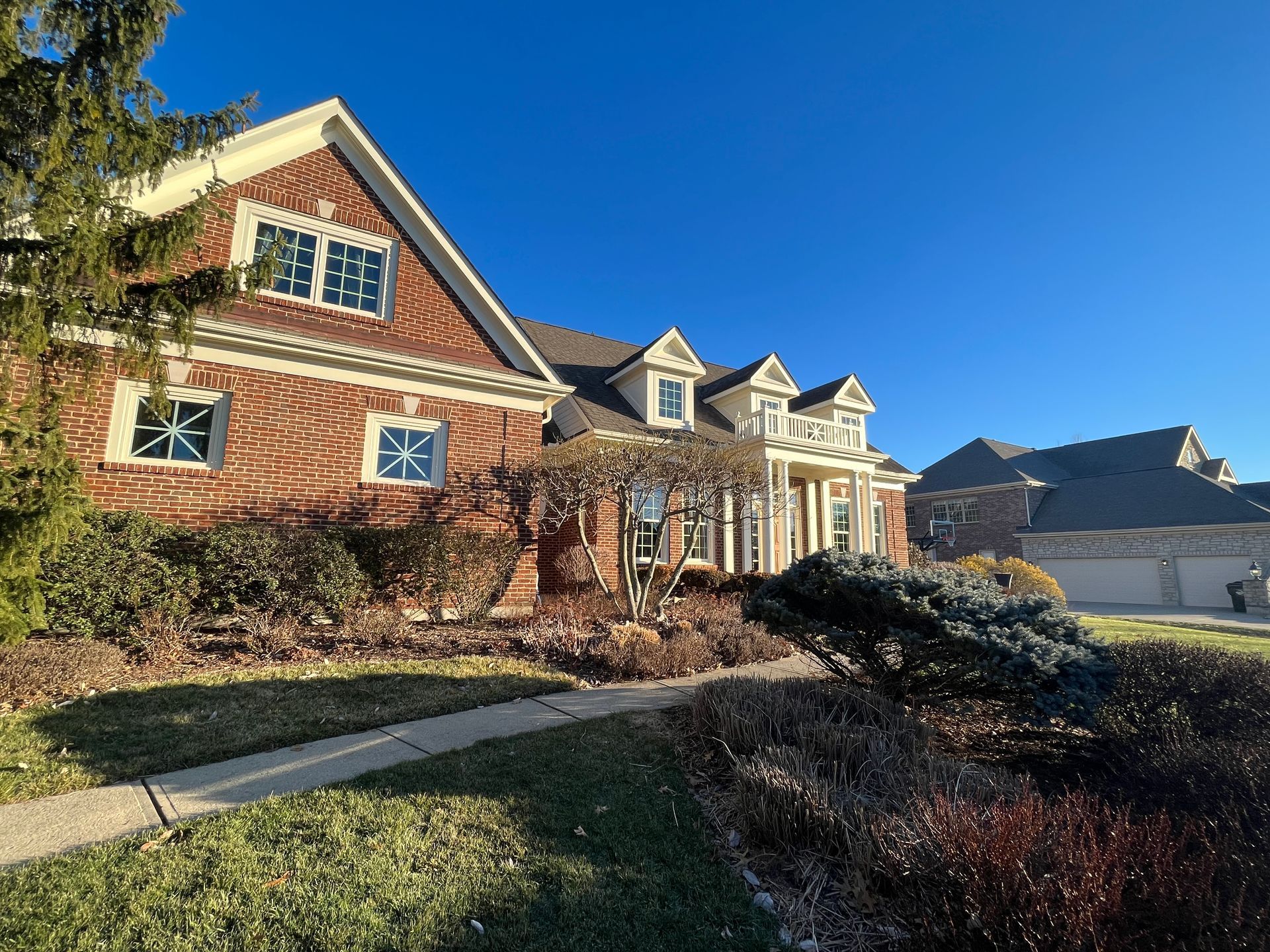 Large brick suburban house with white trim and a manicured front yard on a sunny day