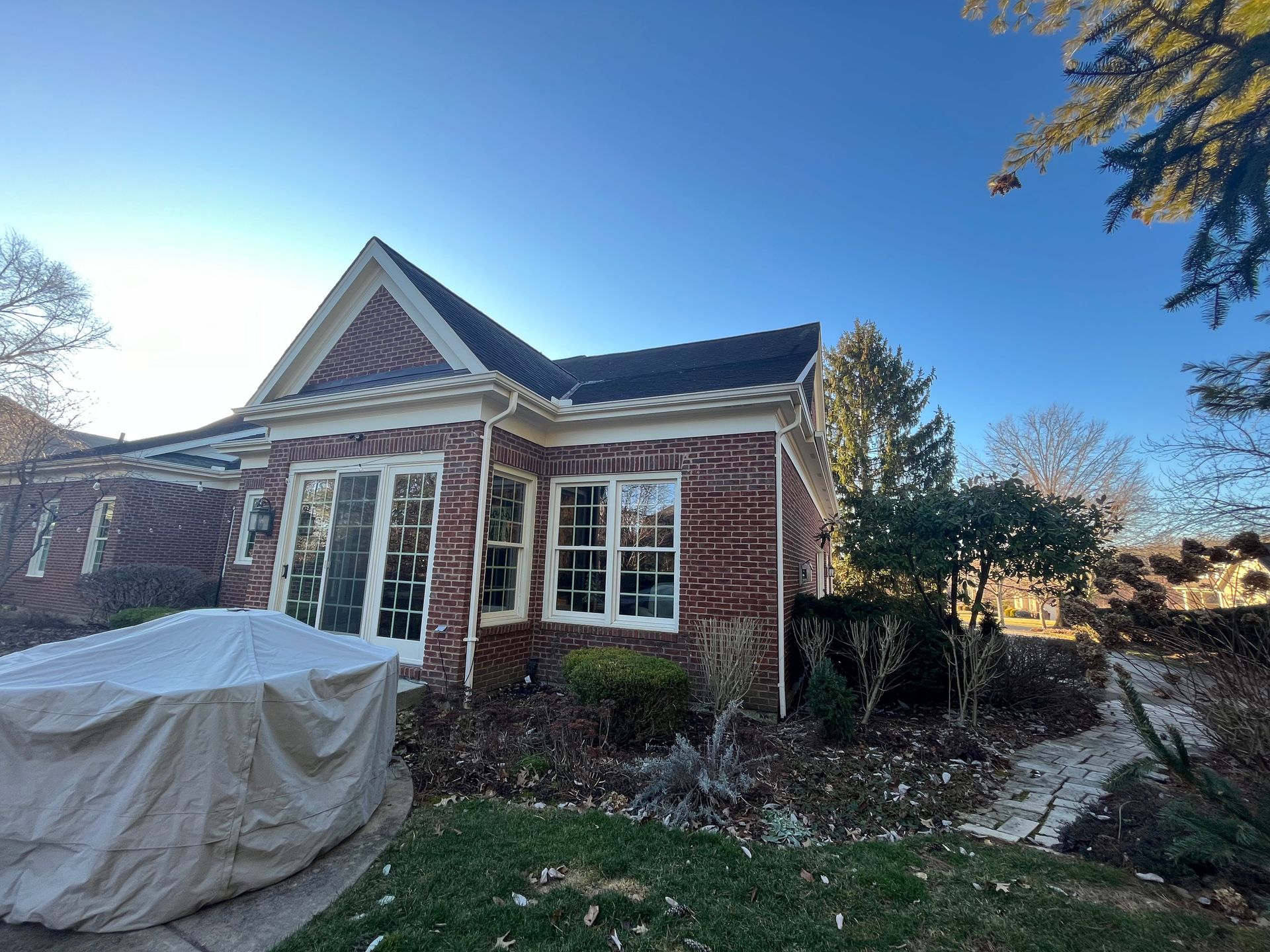 Brick house with white trim and blue roof under a clear sky, with a covered object in the front yard