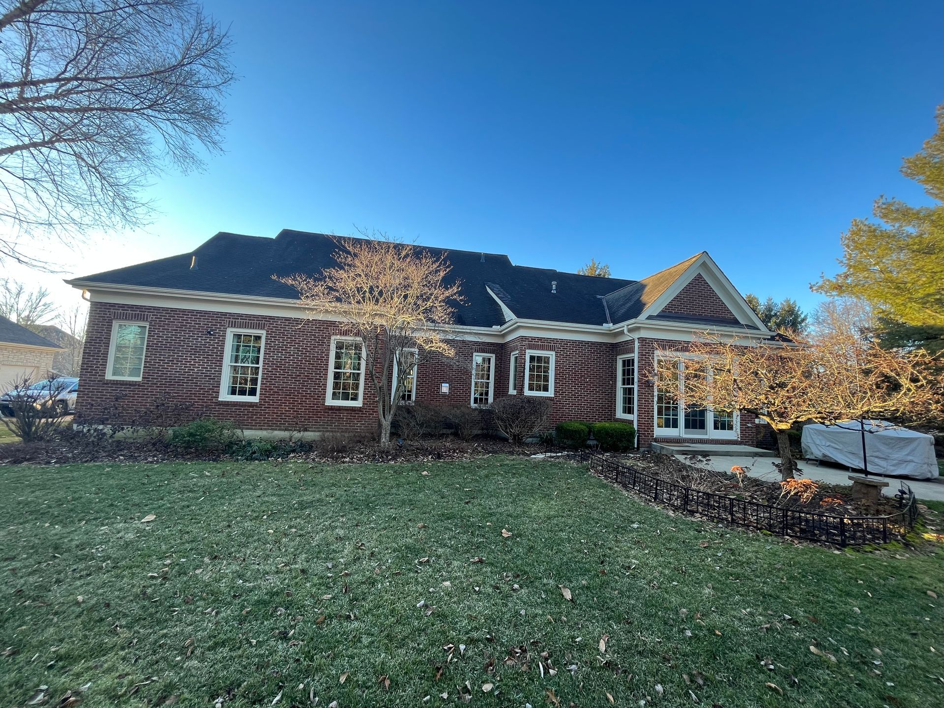 Brick house with dark roof, white-trimmed windows, and a front lawn on a sunny day