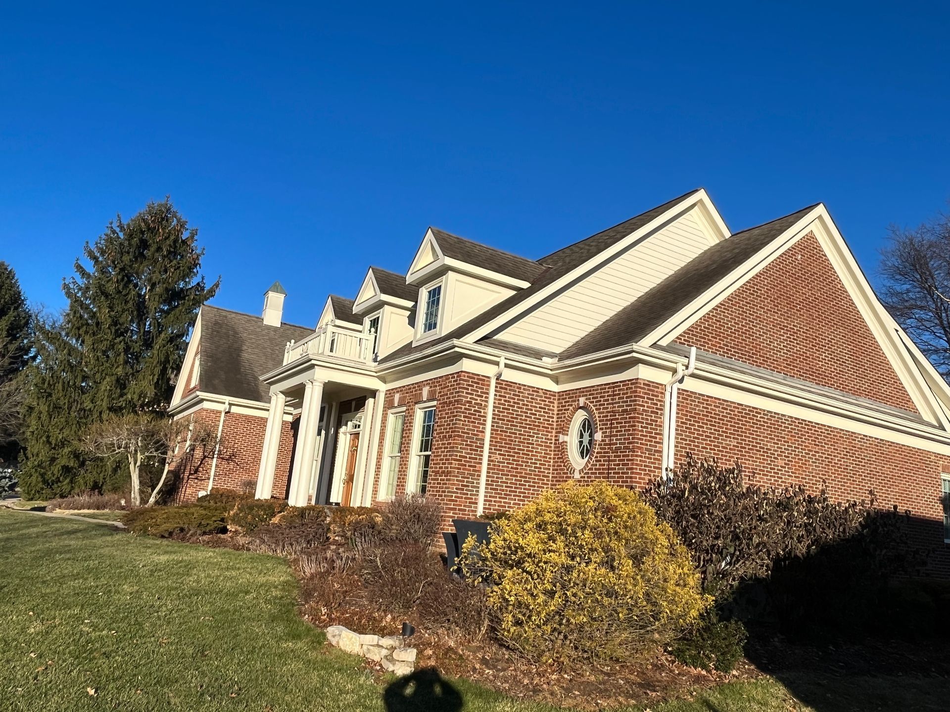 Brick suburban house with steep roof, white trim, and manicured lawn under a clear blue sky