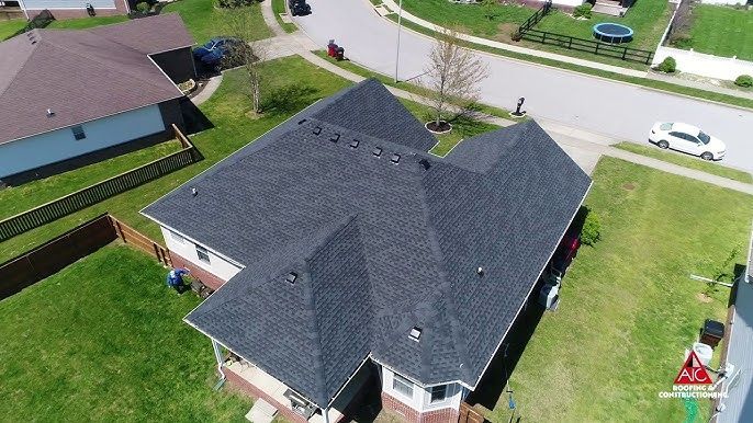 Aerial view of a dark gray-roofed house with a green lawn and suburban street nearby.